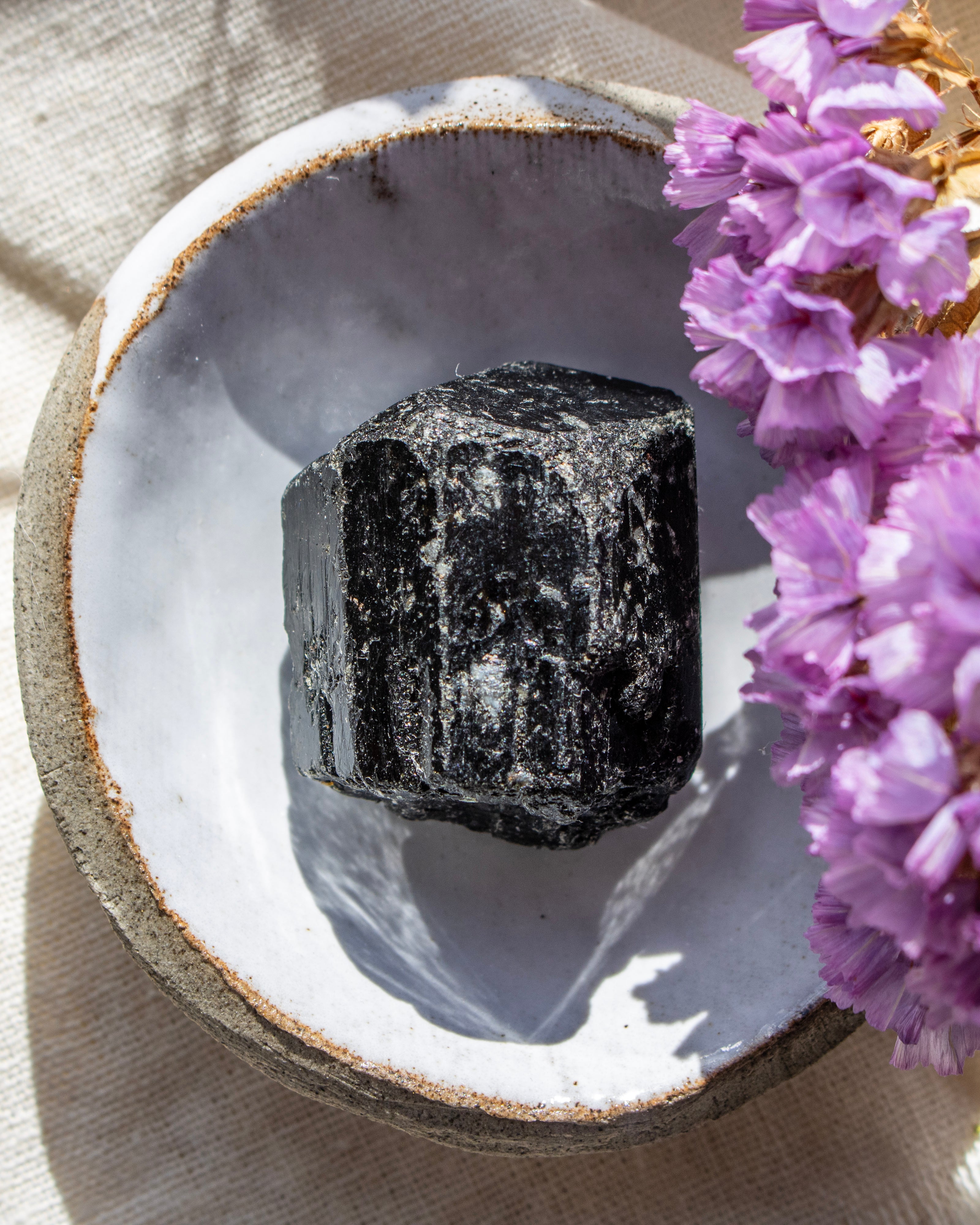 Black crystal on a white stone surface with purple flowers in the background