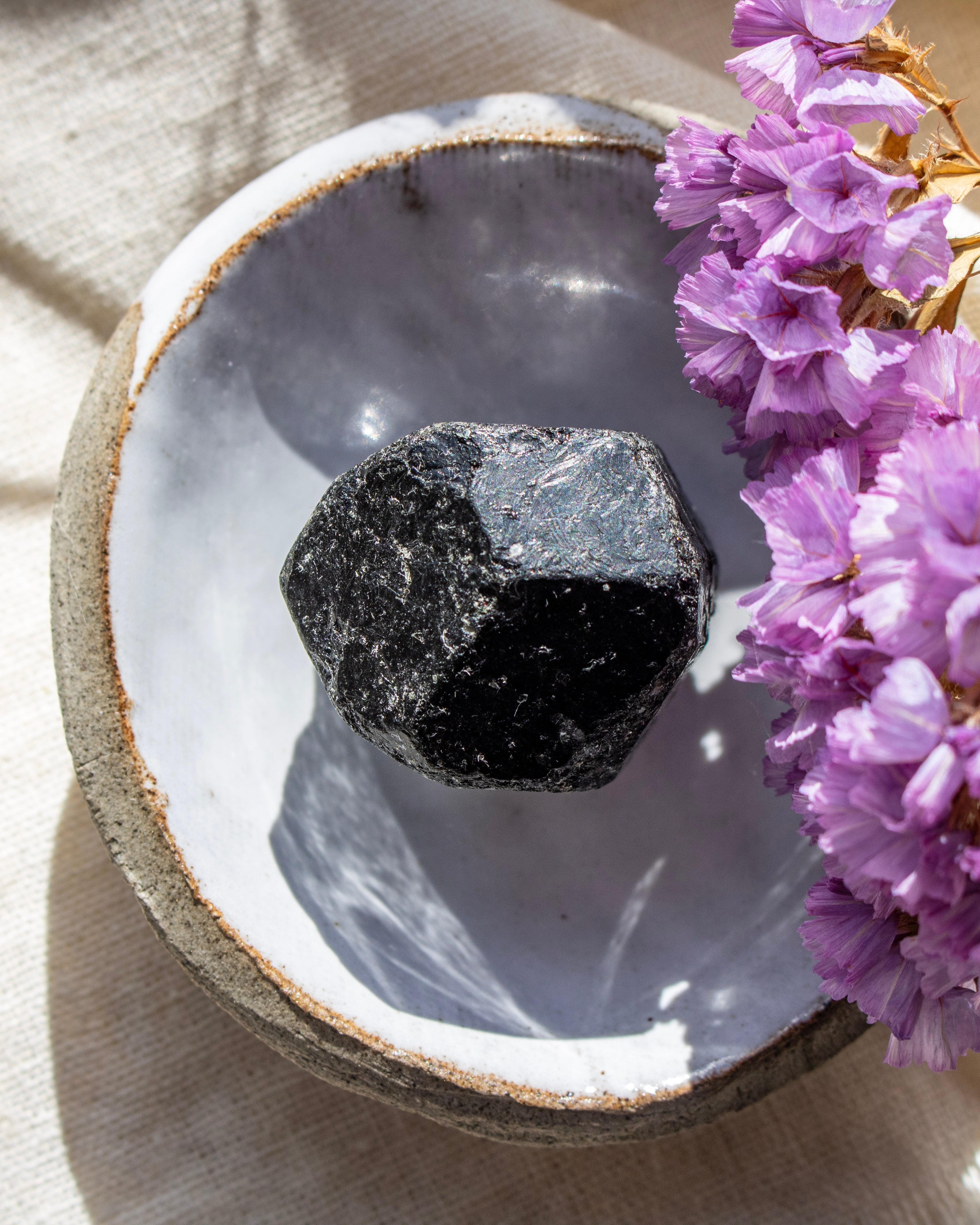 Black stone in a decorative bowl with purple flowers on a light background