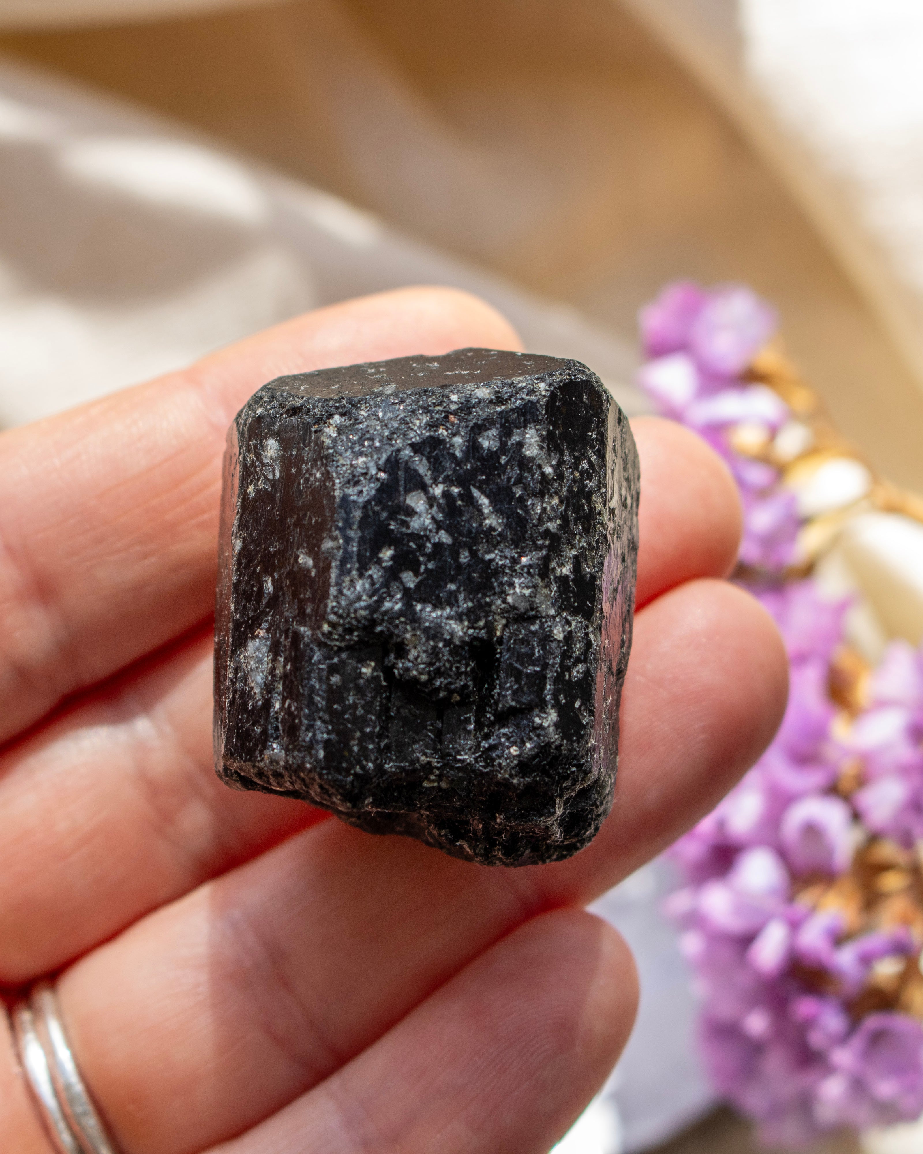 Hand holding a dark crystal with blurred purple flowers in the background