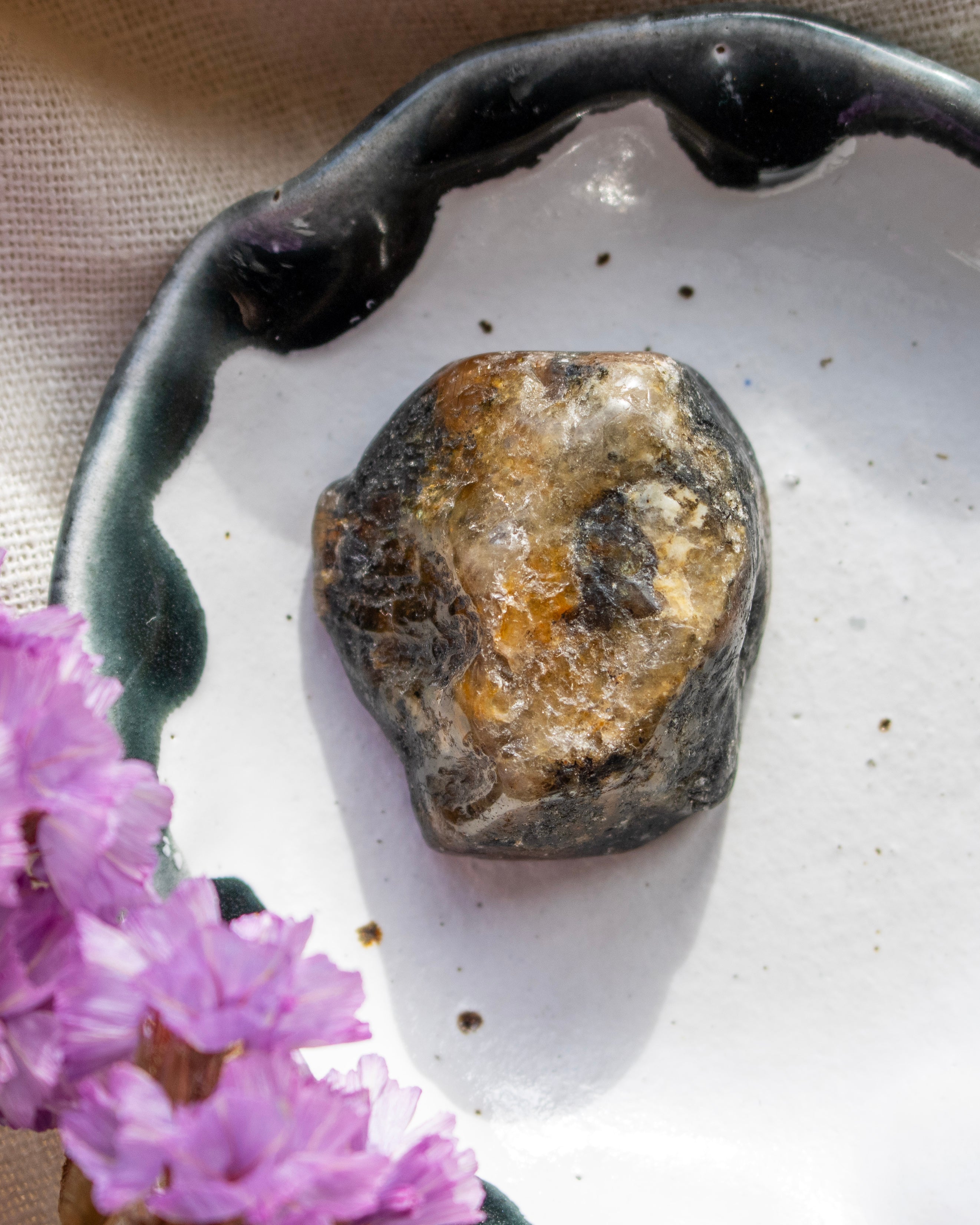 Rustic dish with a textured stone and purple flowers on a beige background