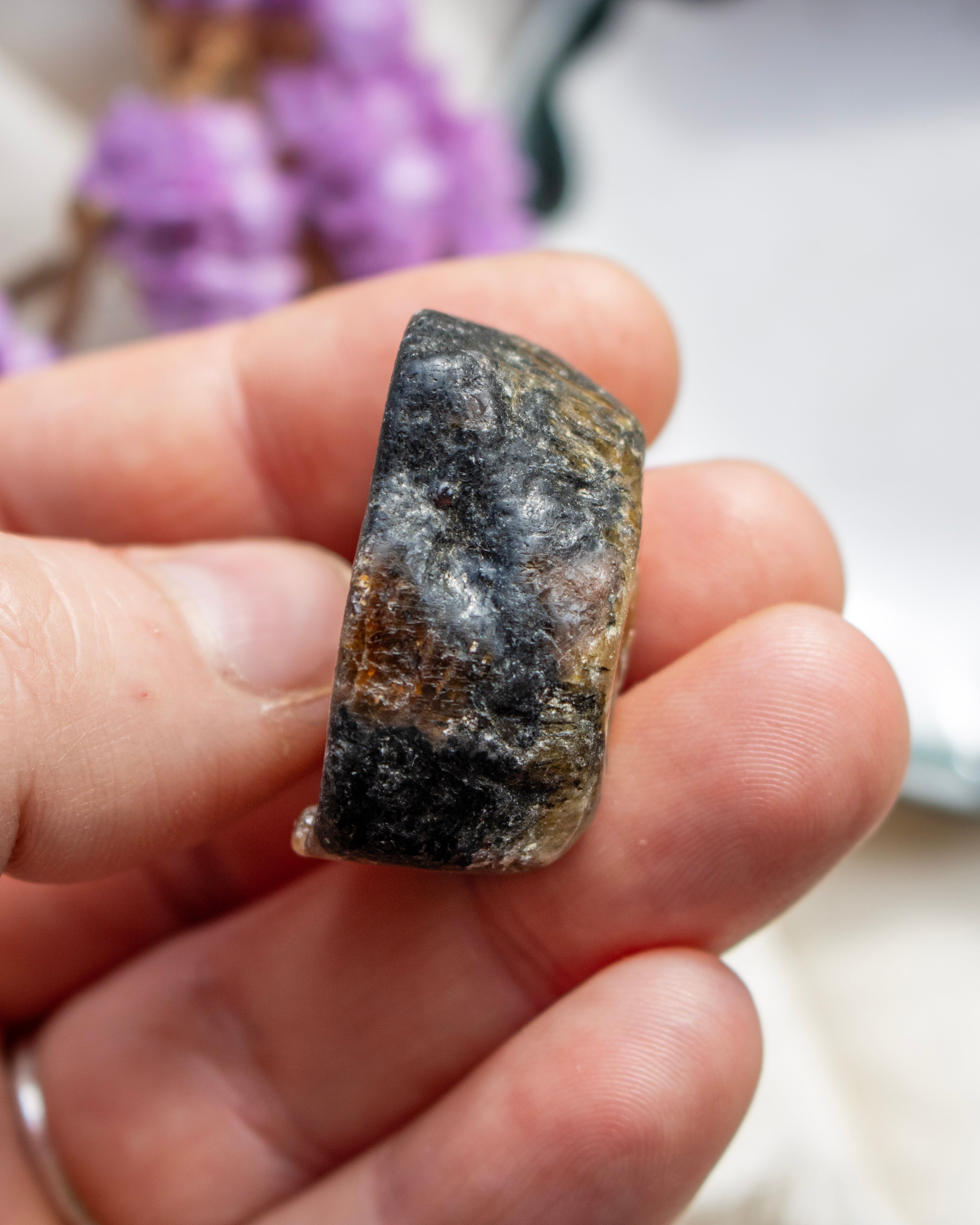 Hand holding a rough stone with a blurred purple flower in the background