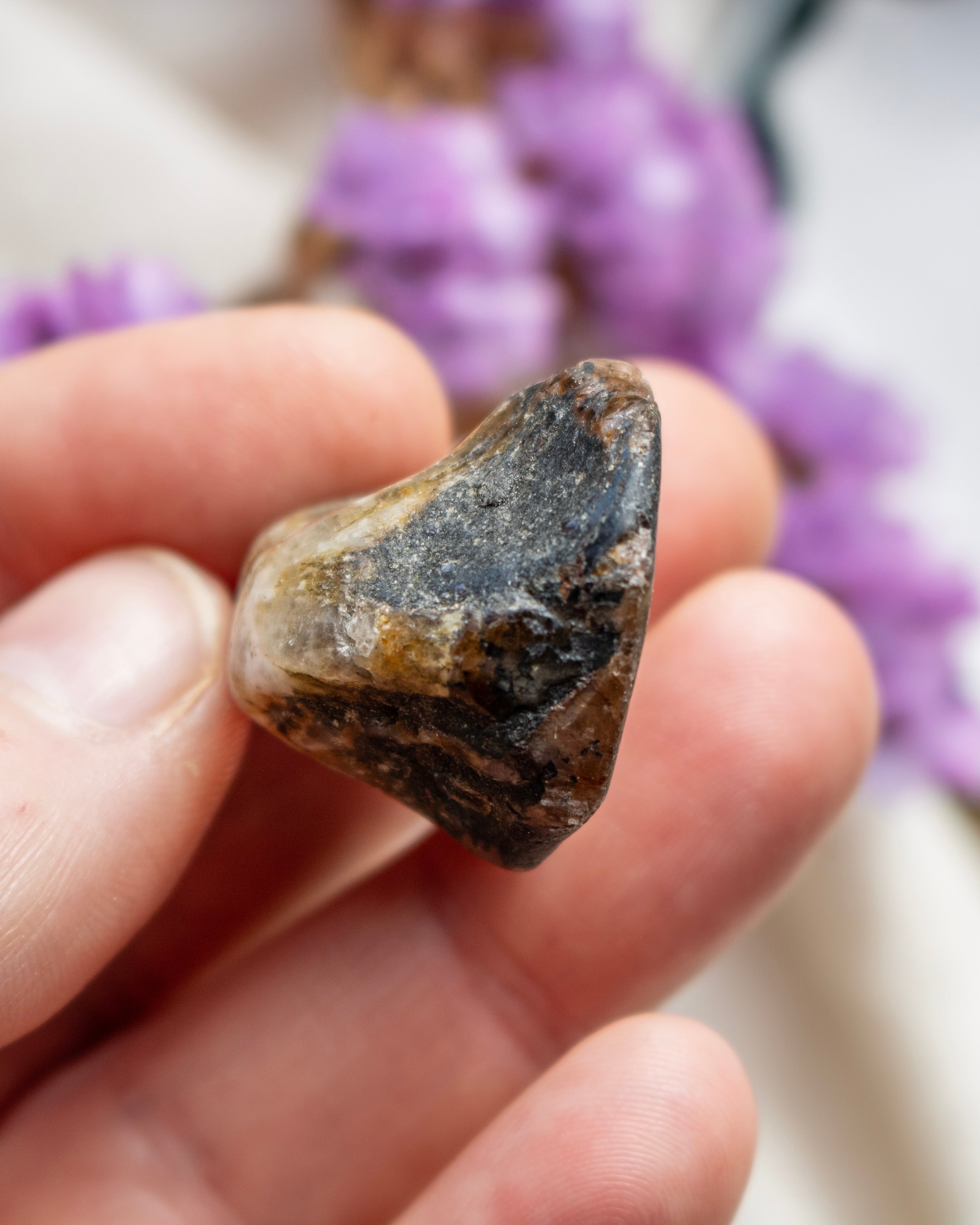 Mineral stone held between fingers with blurred purple flowers in the background