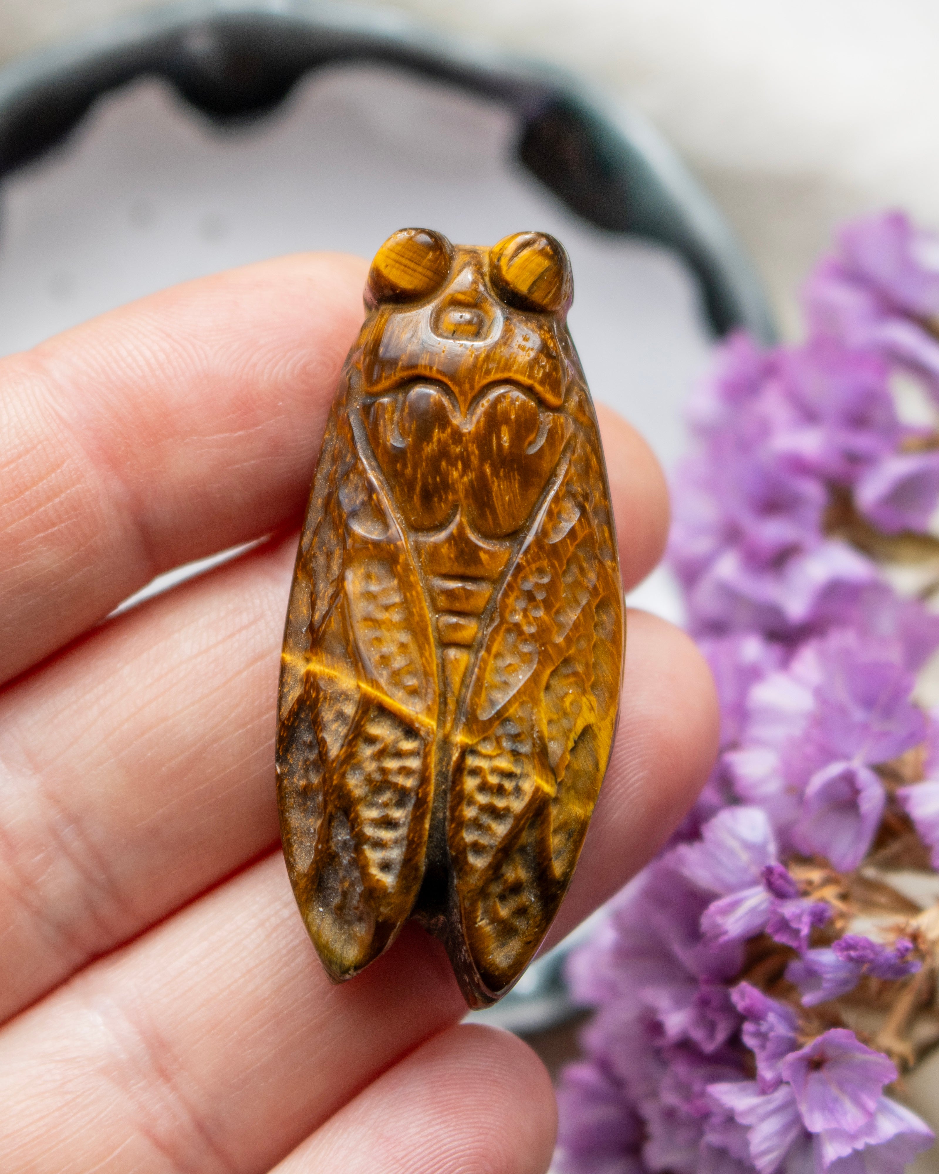 Carved stone insect held in a hand with purple flowers in the background