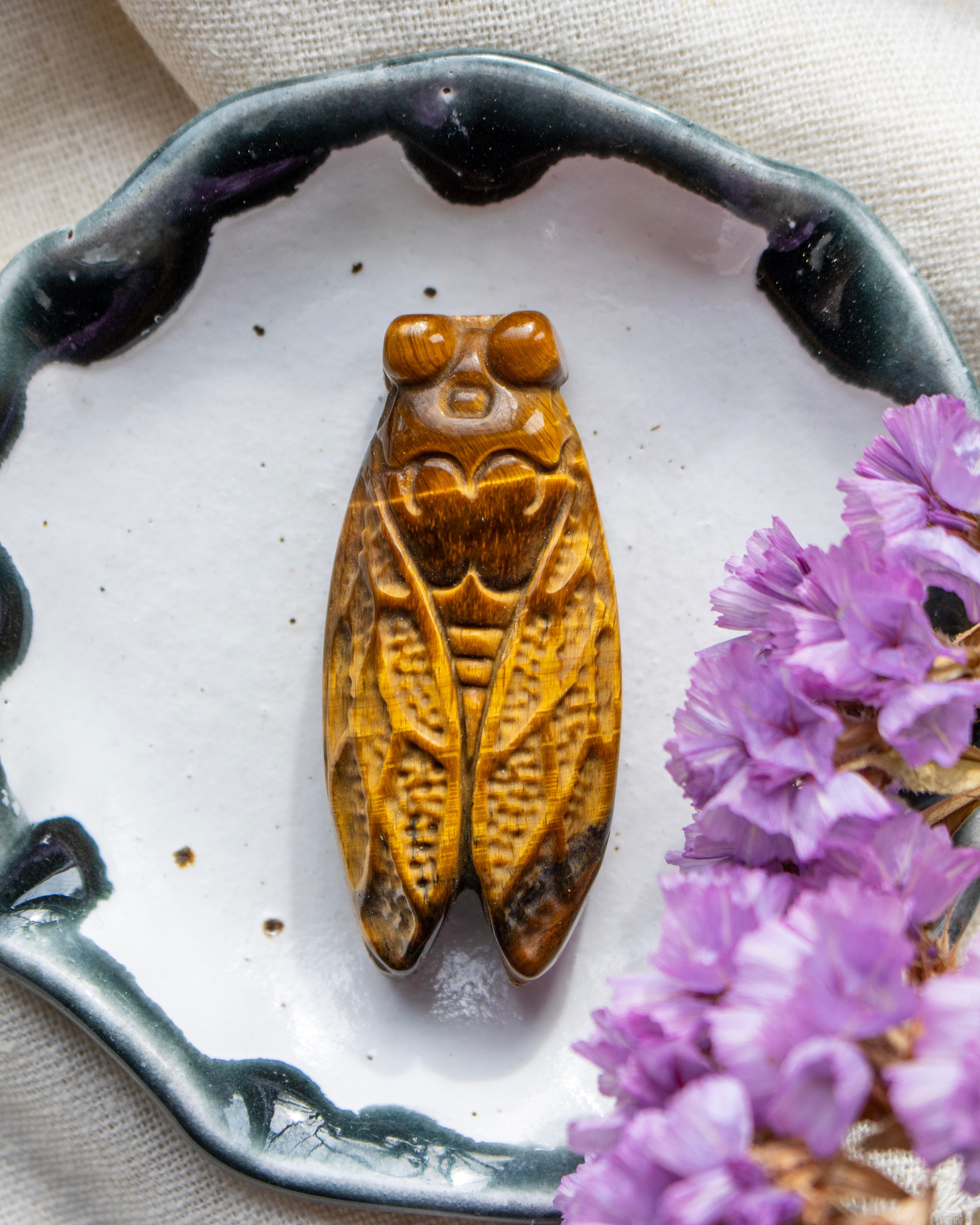 Carved stone cicada on a white plate with purple flowers