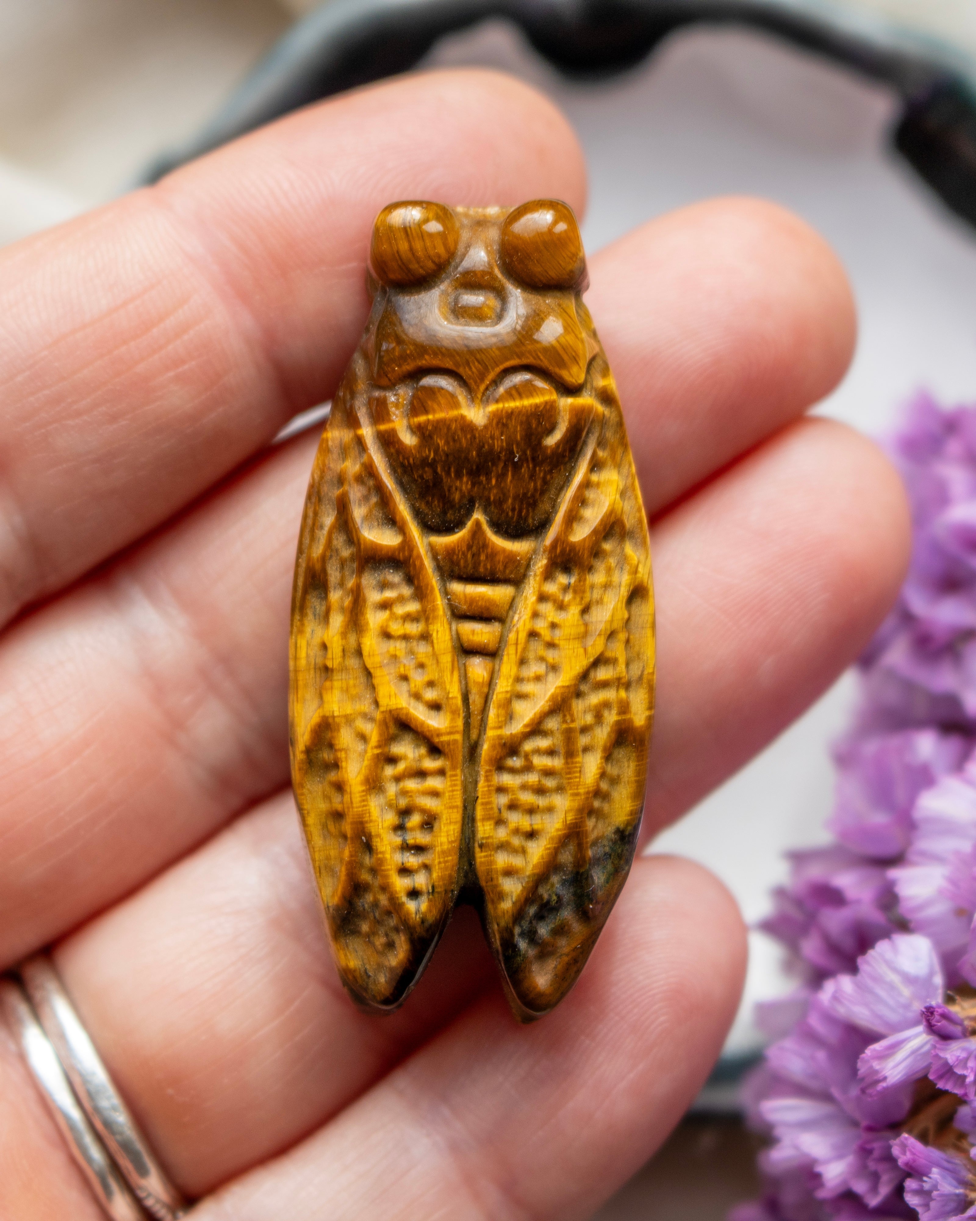 Carved crystal insect pendant held between fingers with a blurred background
