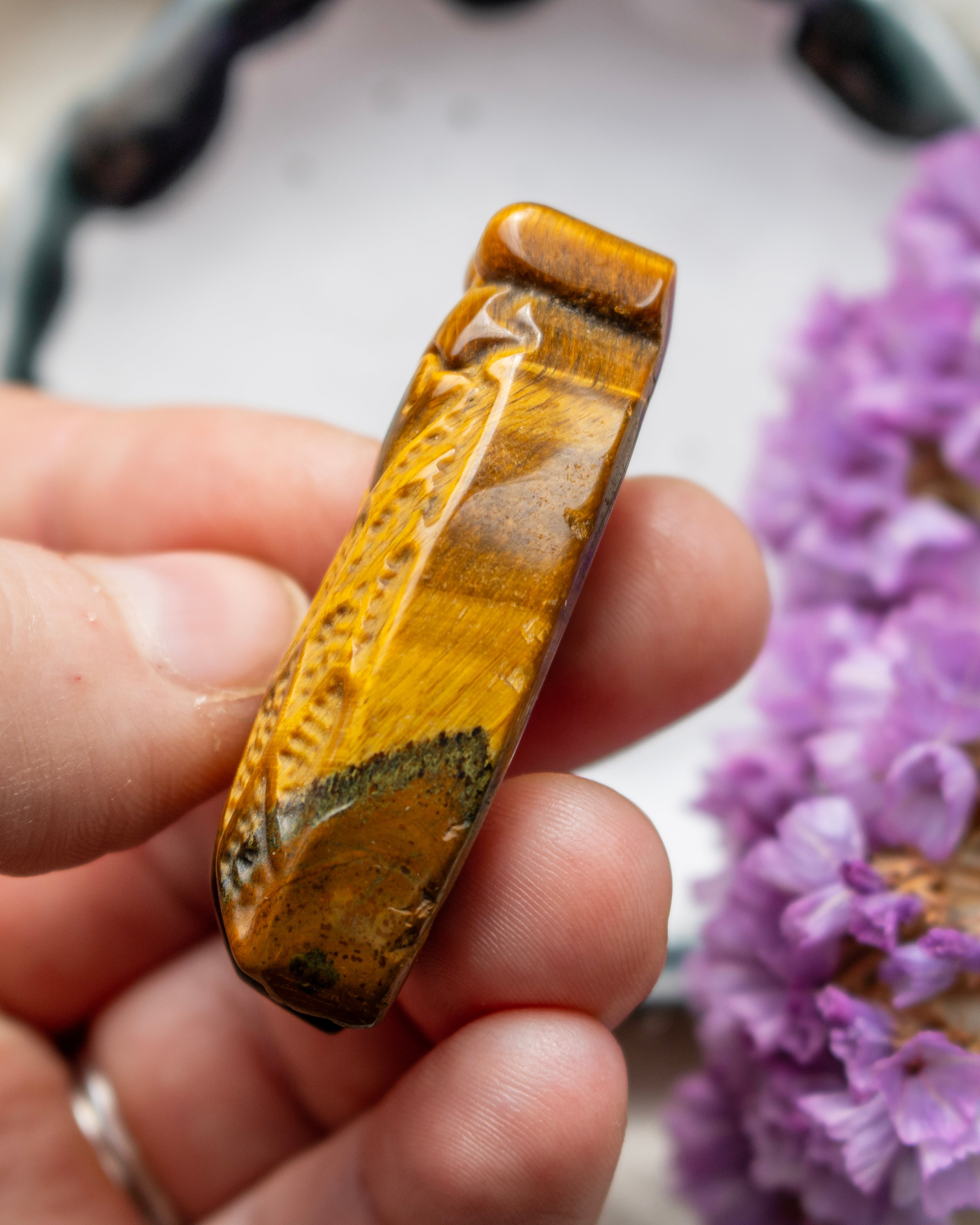 Hand holding a tiger's eye crystal with purple flowers in the background