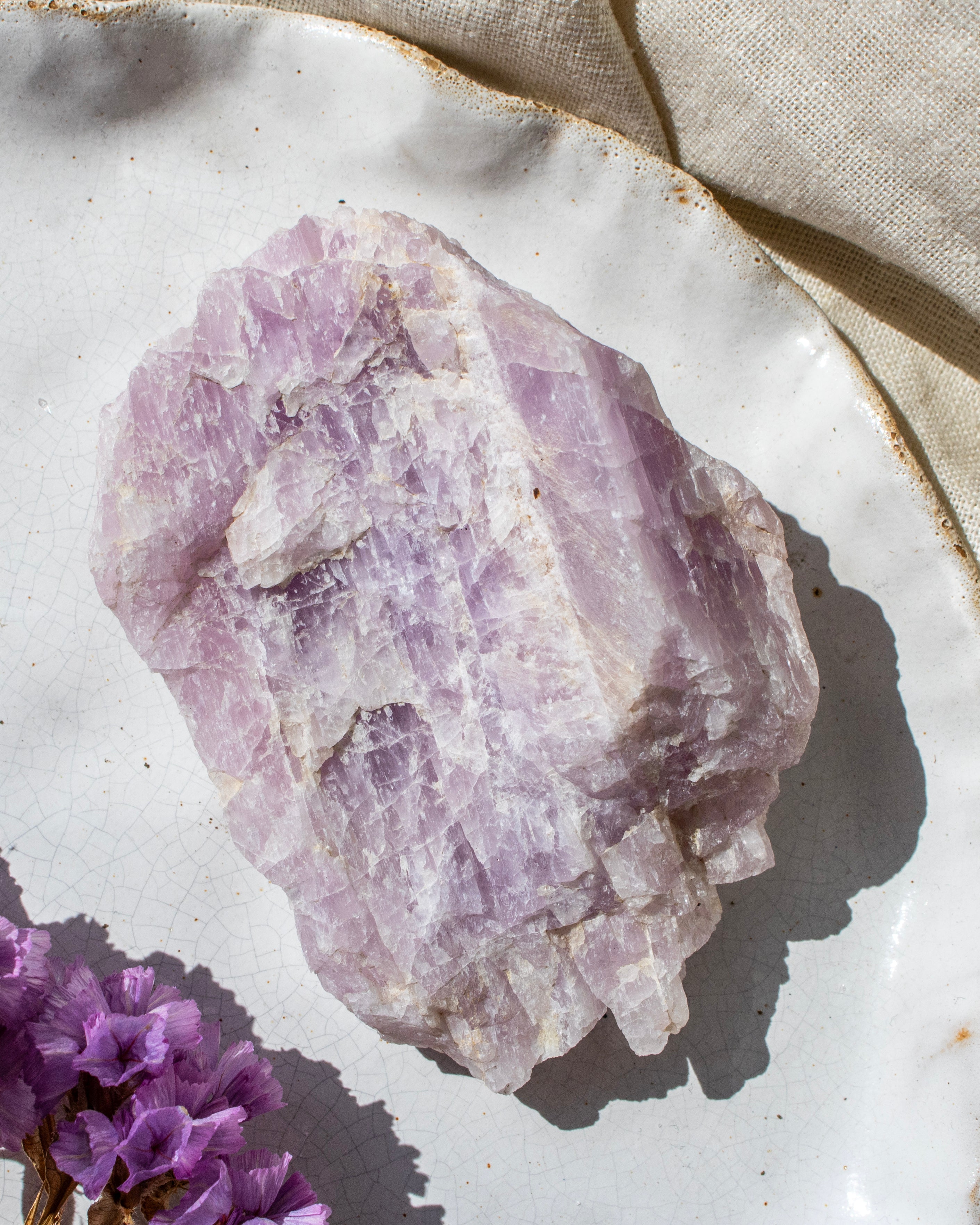 Raw kunzite crystal on a white surface with a beige cloth in the background