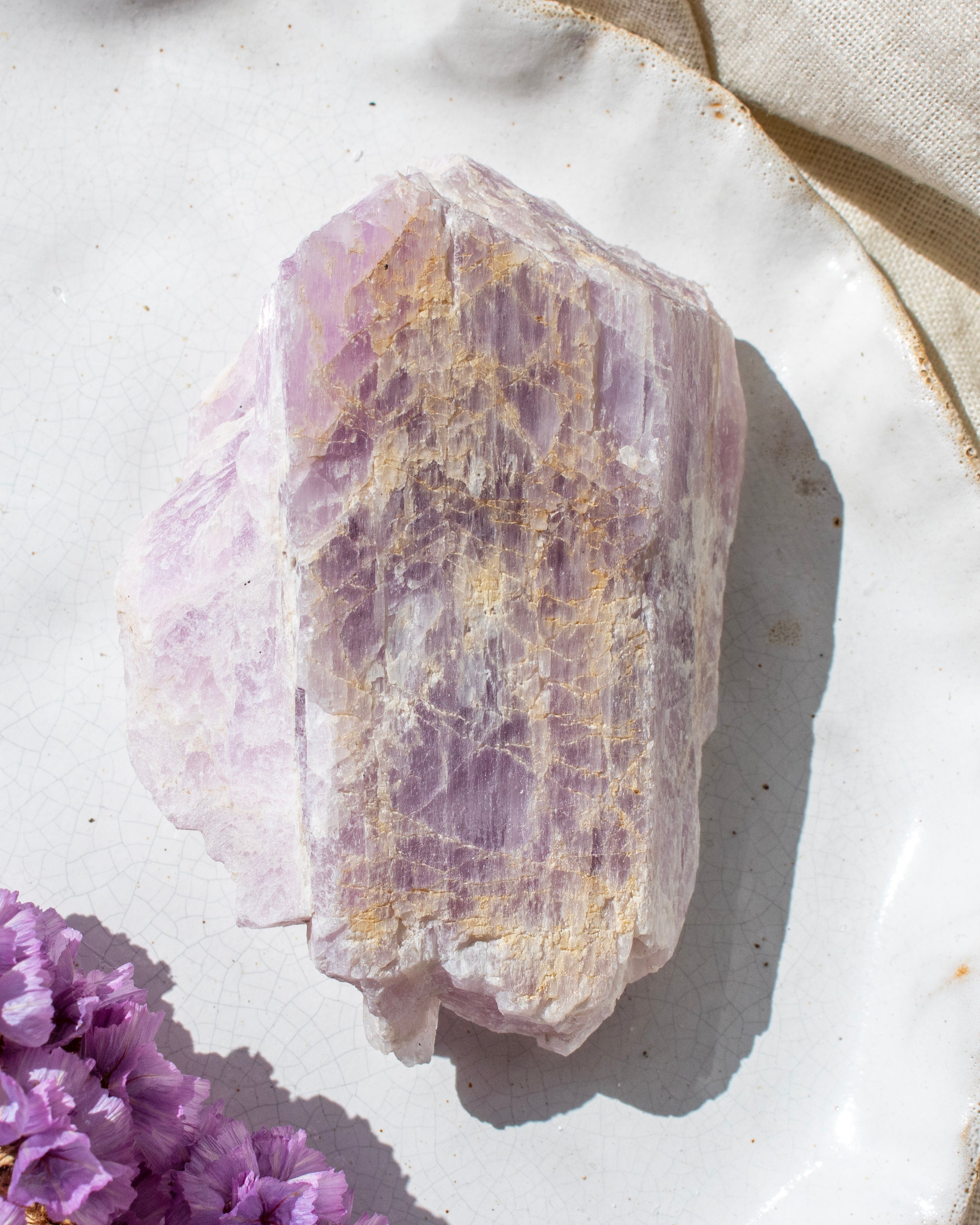 Raw kunzite crystal on a white surface with purple flowers