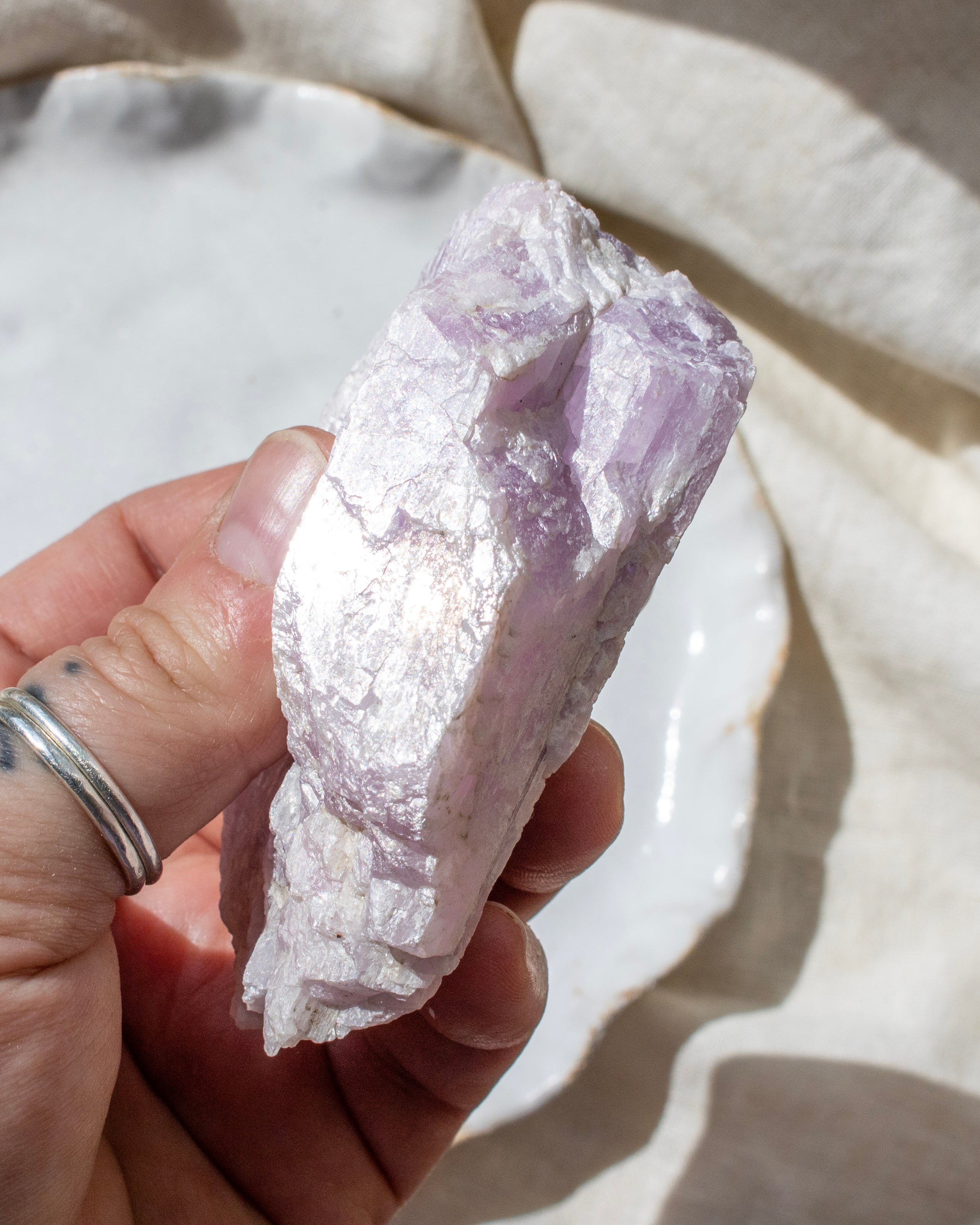Hand holding a rough kunzite crystal against a neutral background