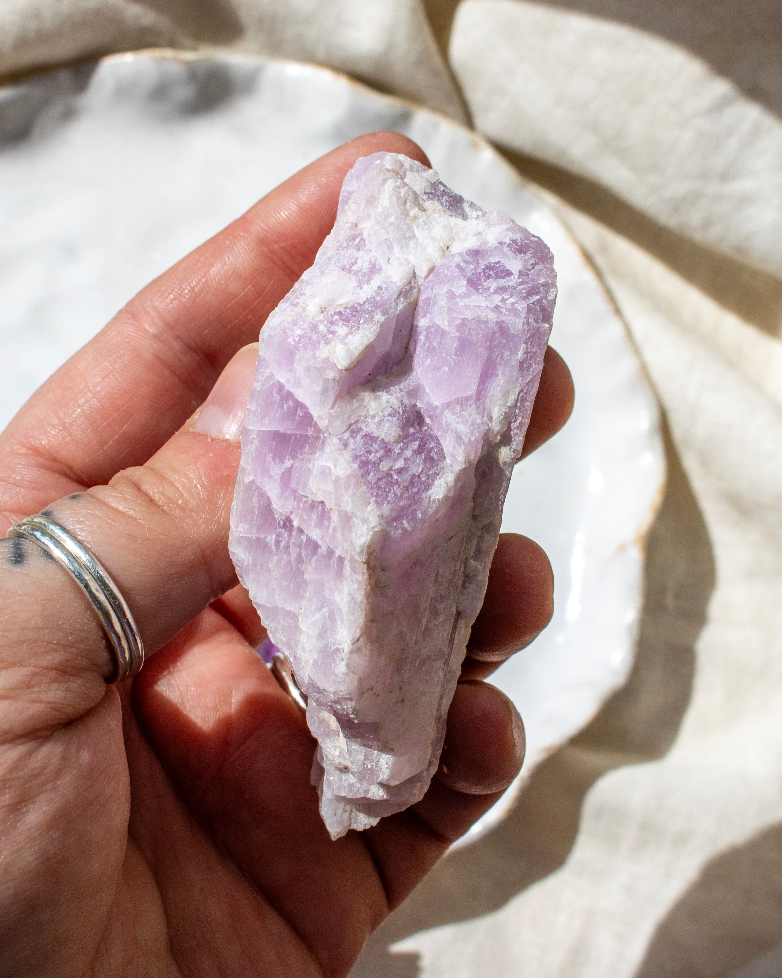 Hand holding a purple crystal against a neutral background