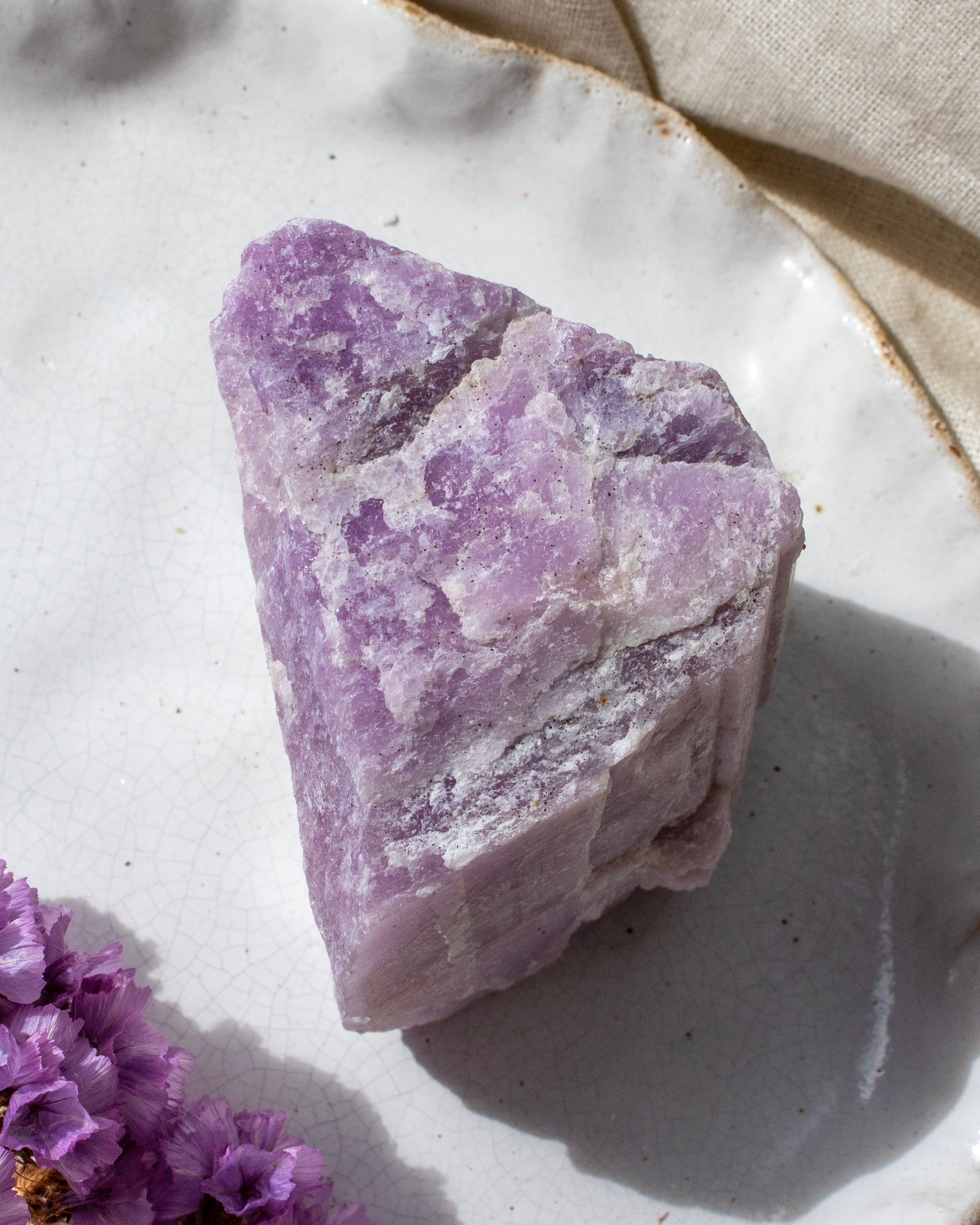 Purple crystal on a white surface with a beige cloth in the background