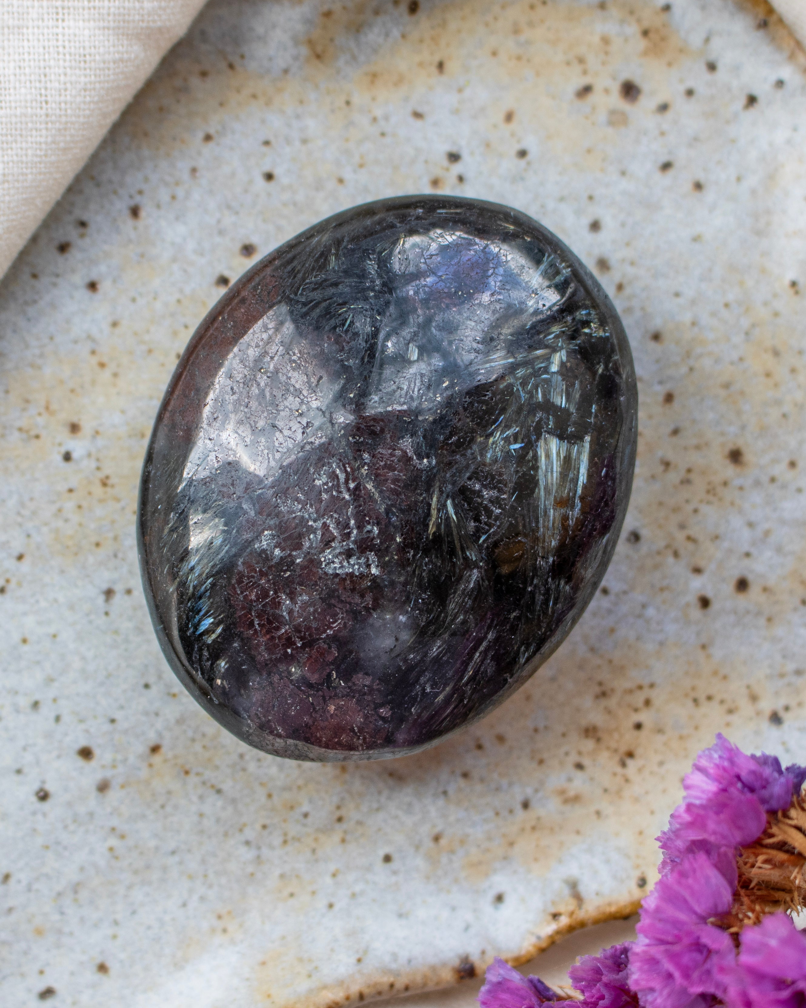 Polished dark brown stone on a textured surface with purple flowers
