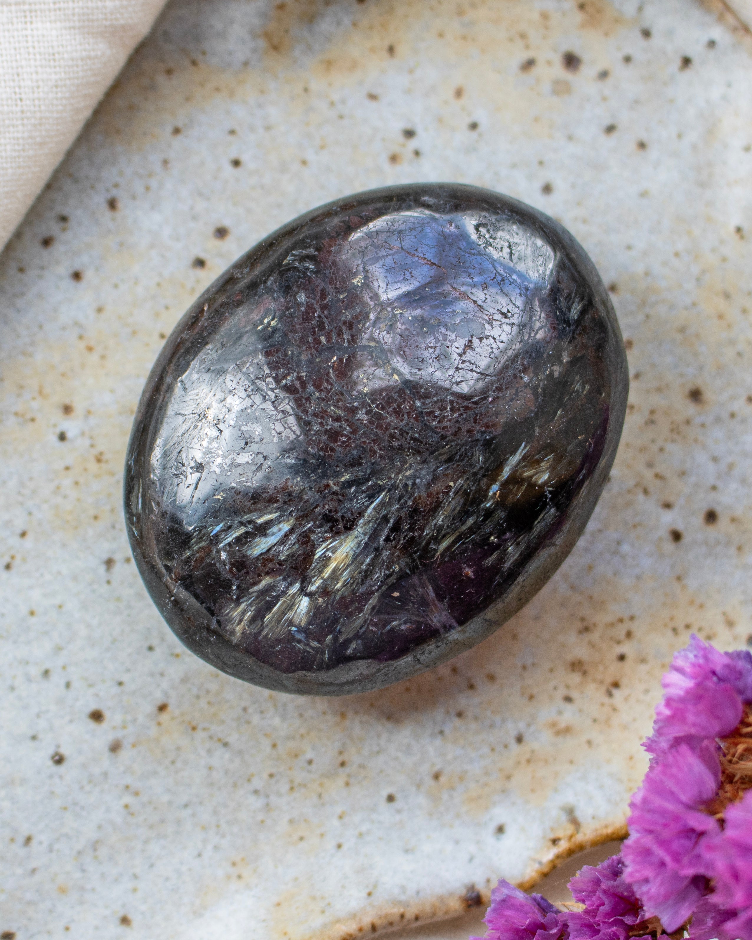 Polished gemstone on a textured surface with a pink flower