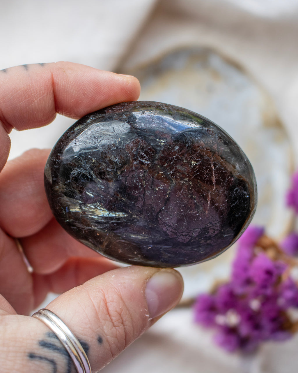 Hand holding a dark stone with a blurred background featuring purple flowers