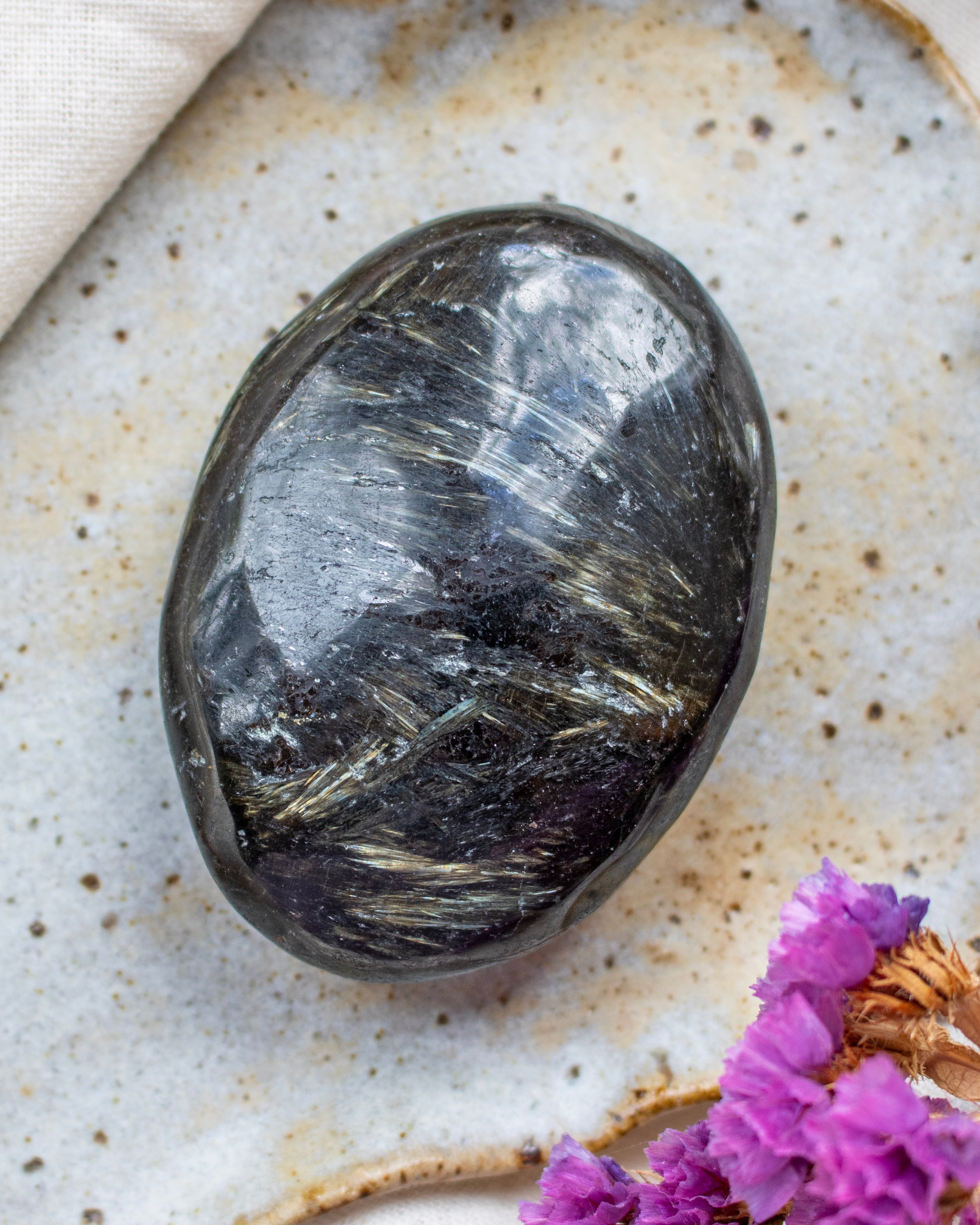 Polished stone on a textured surface with purple flowers