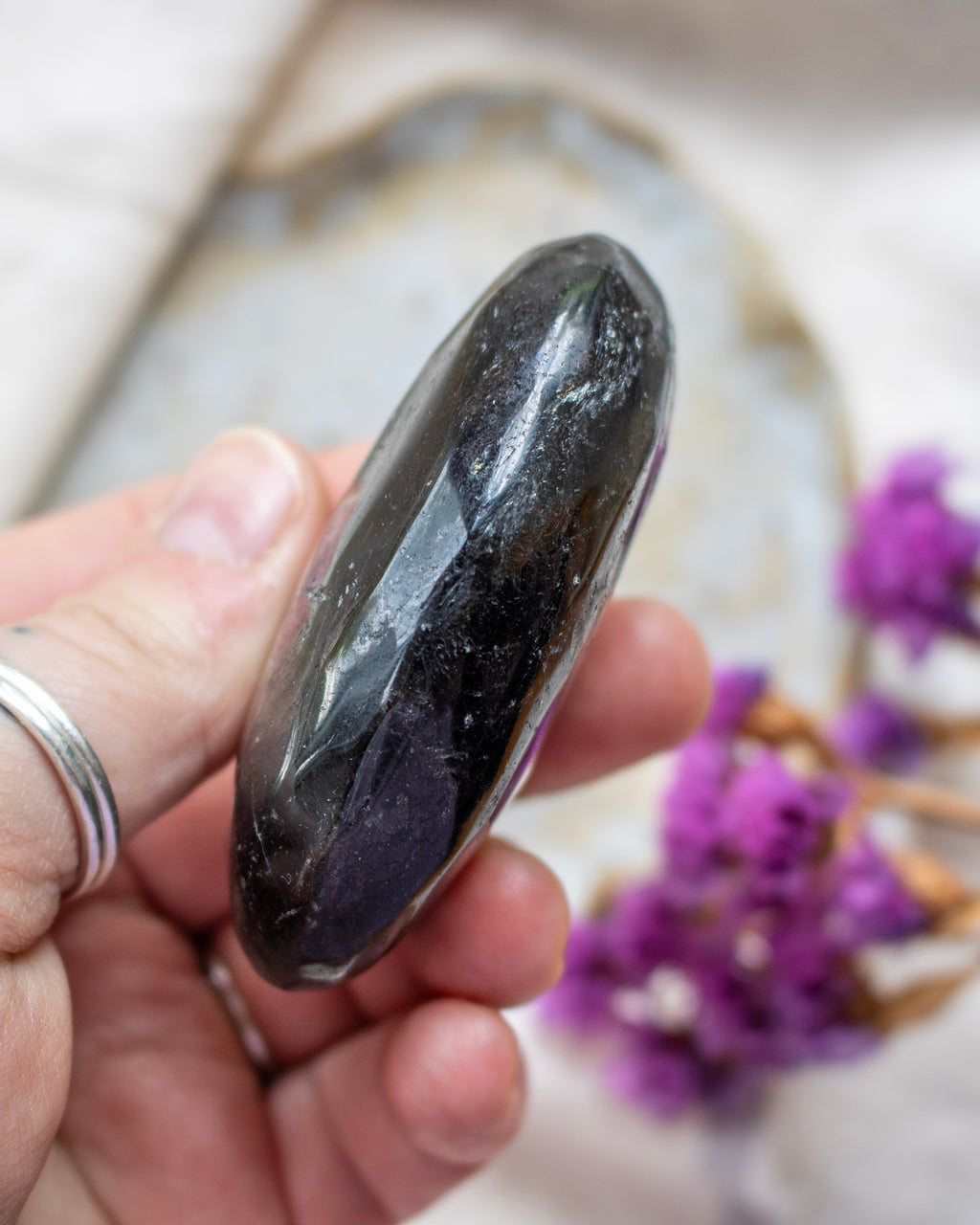 Hand holding a dark stone with blurred purple flowers in the background