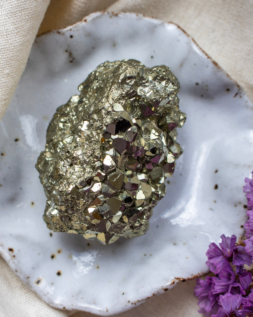 Pyrite crystal on a white speckled surface with purple flowers