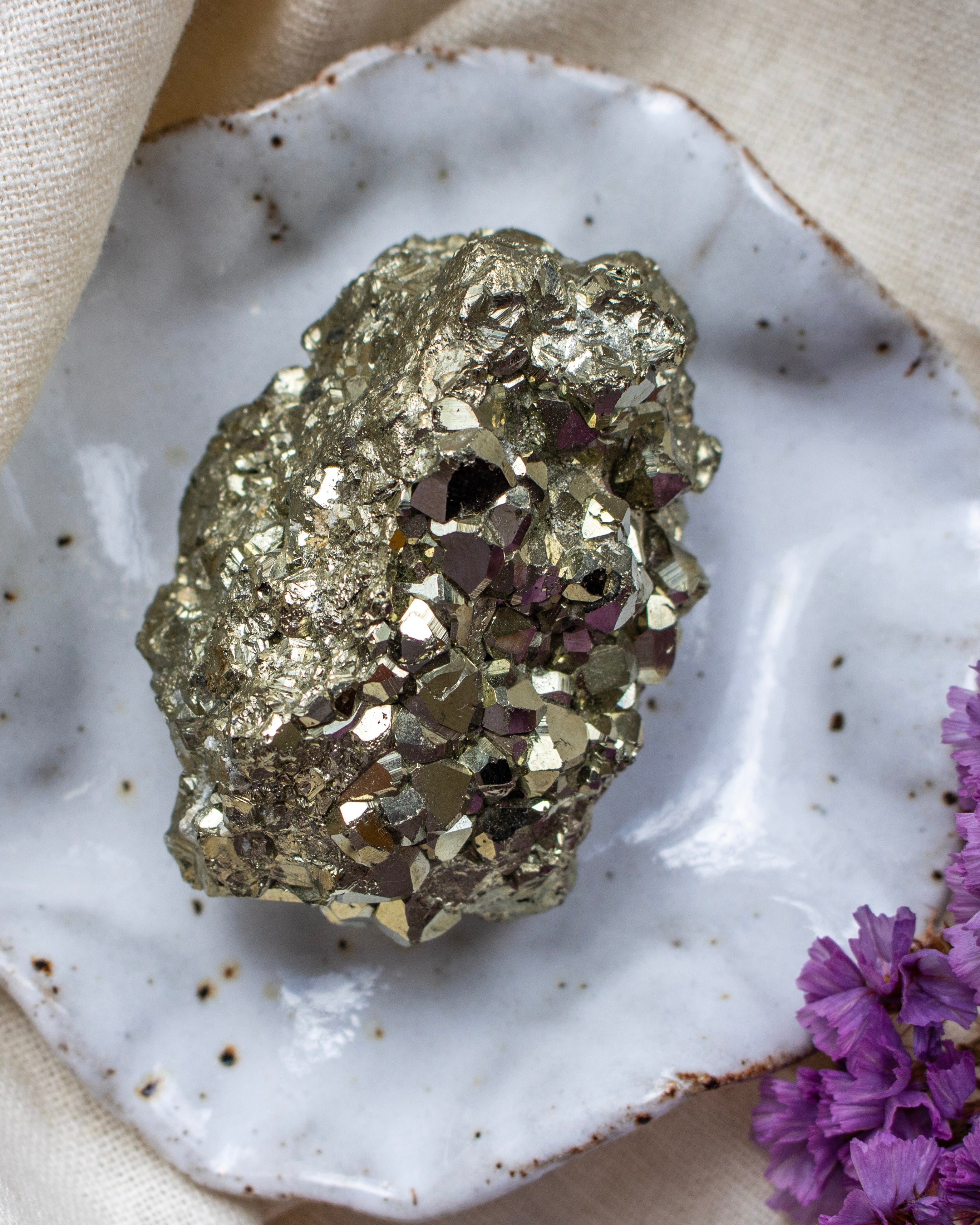 Pyrite crystal on a white speckled surface with purple flowers