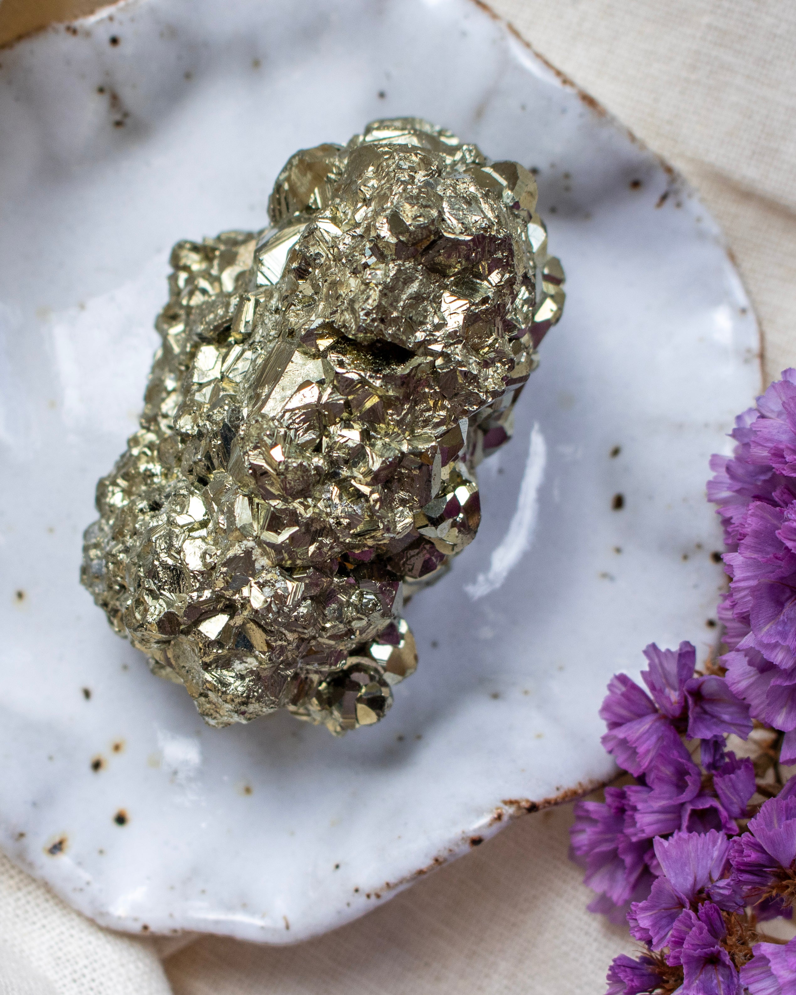 Gold pyrite crystal on a white ceramic plate with purple flowers