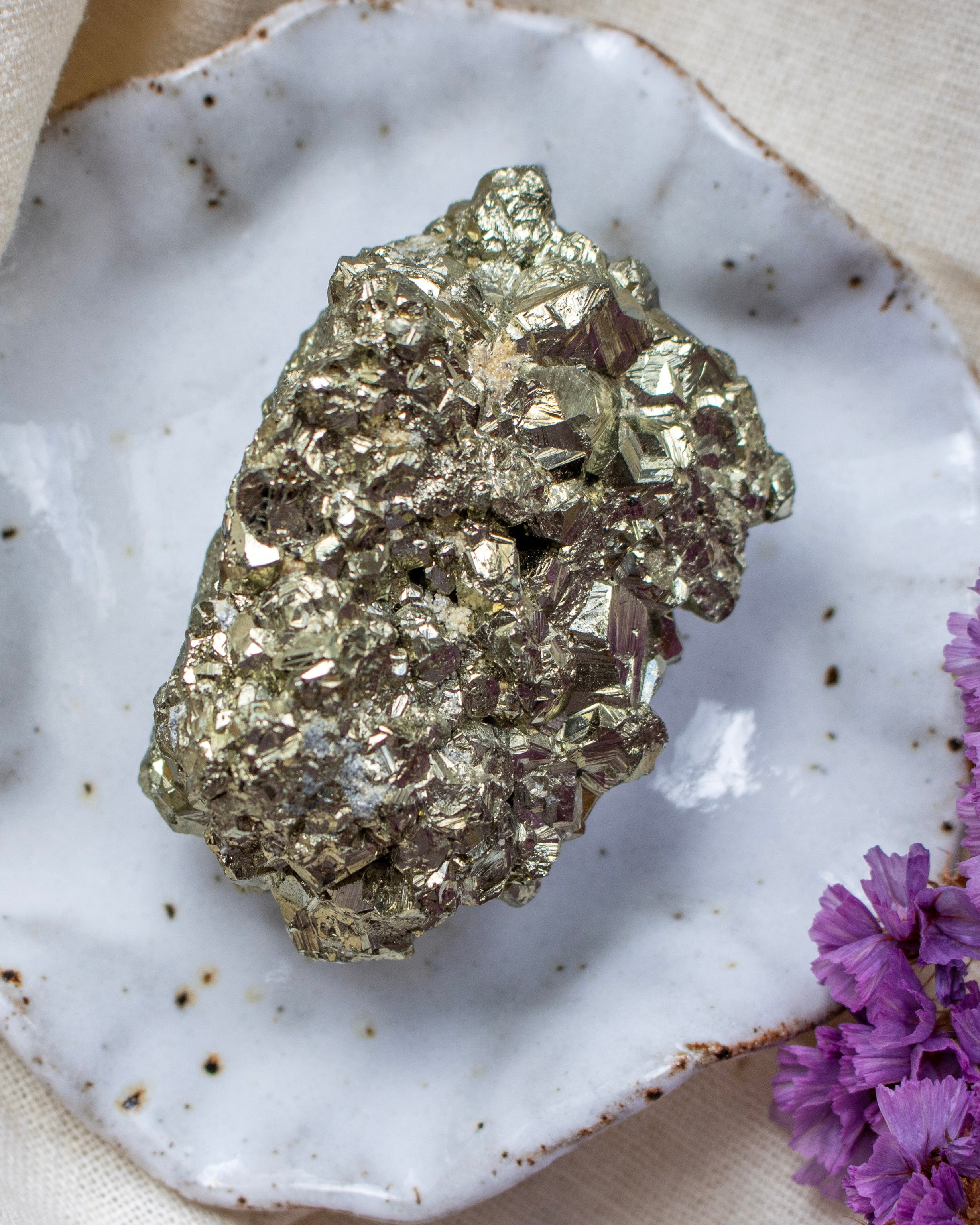 Pyrite crystal on a speckled ceramic plate with purple flowers