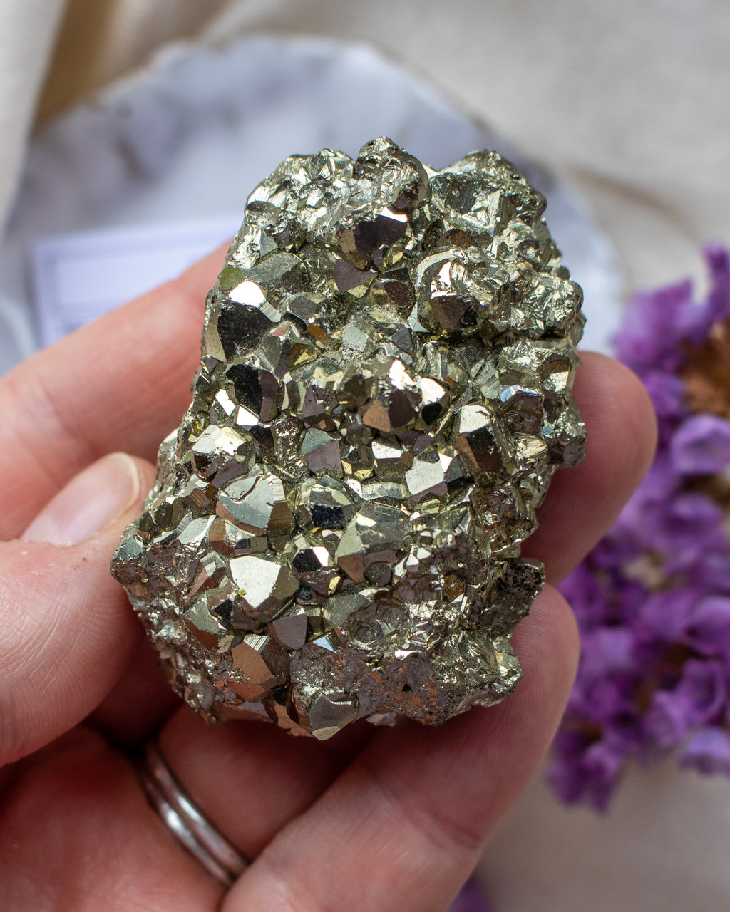Hand holding a large pyrite crystal with purple flowers in the background