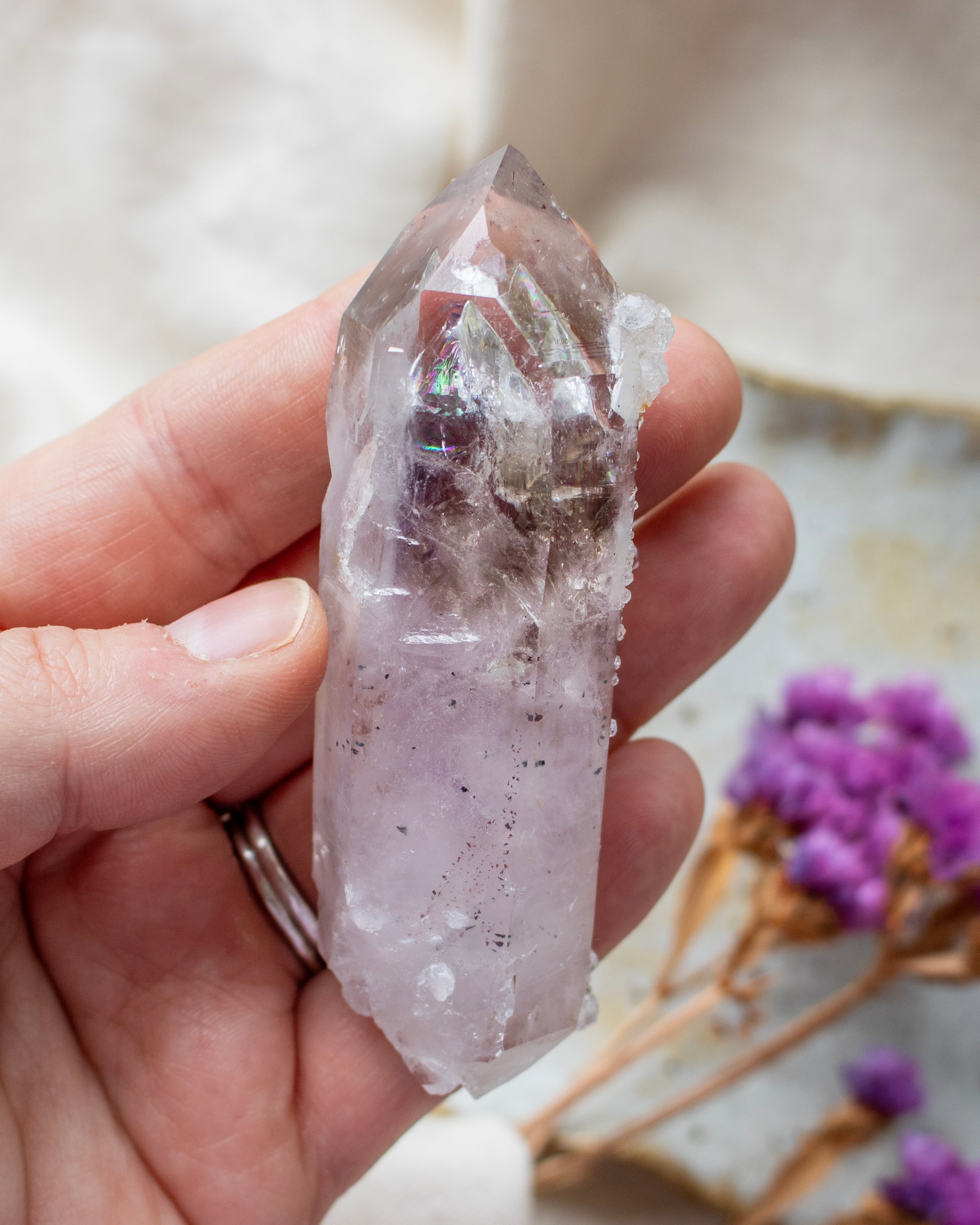 Hand holding a clear crystal with purple flowers in the background