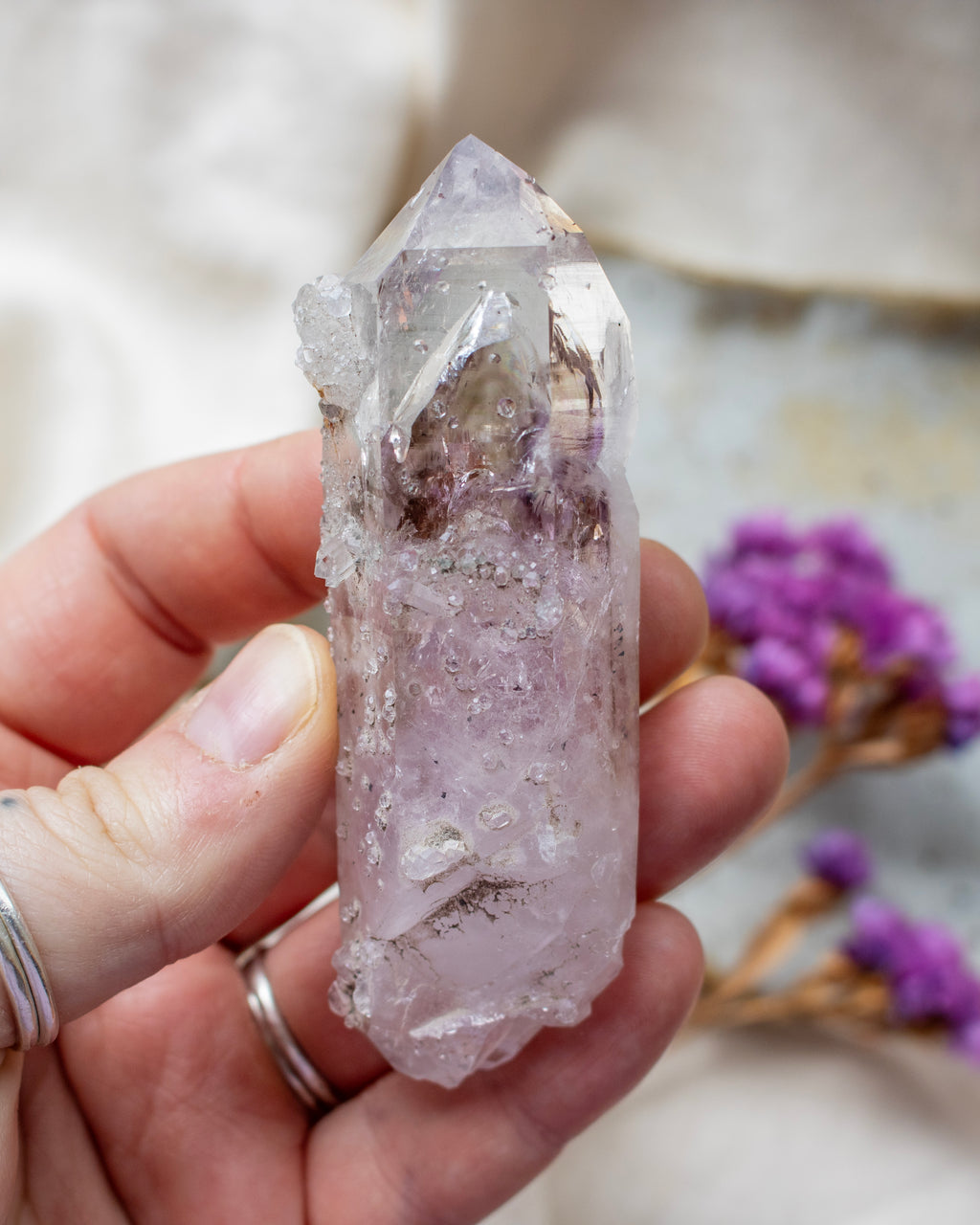 Hand holding a clear crystal with purple flowers in the background