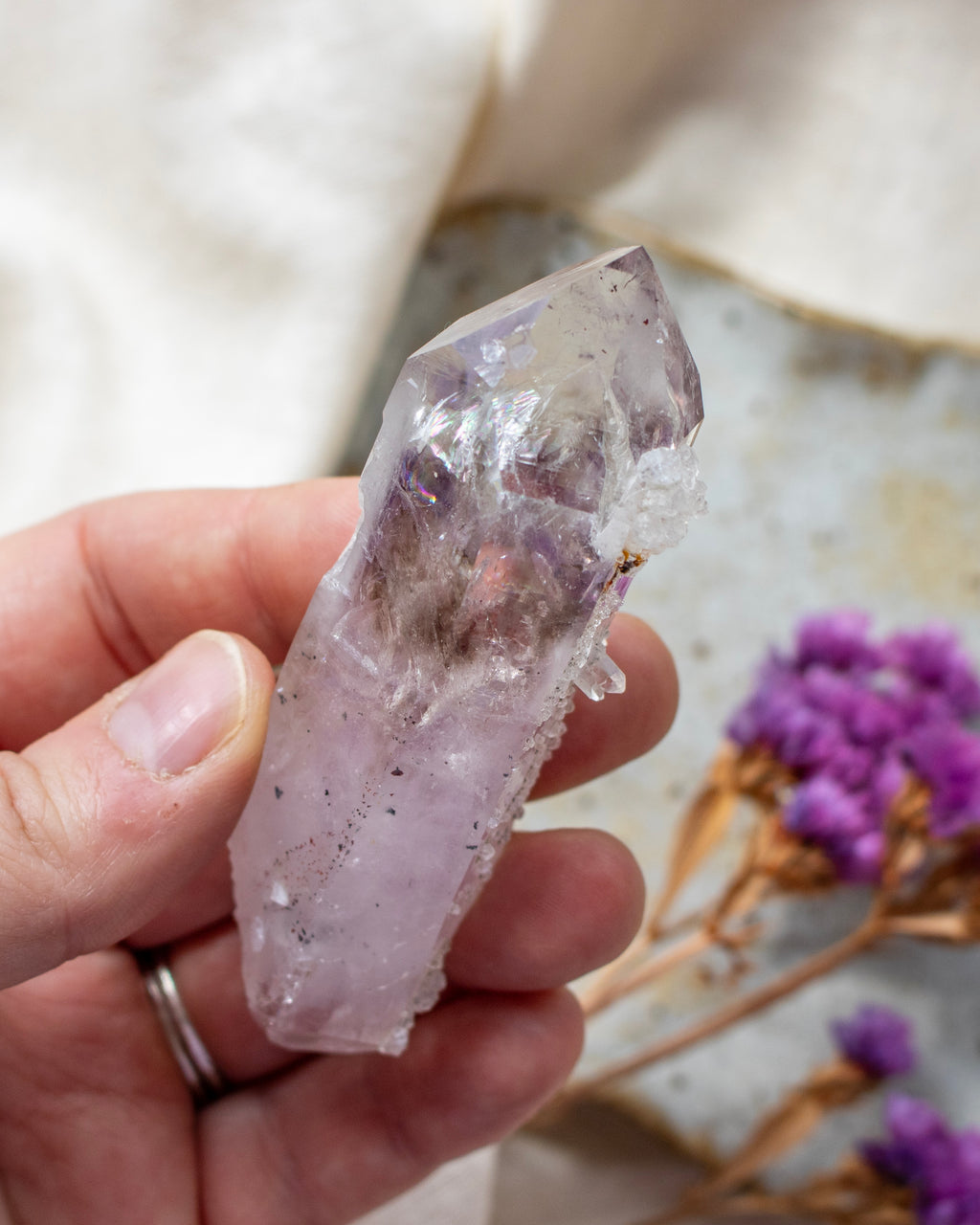 Hand holding a clear crystal with purple accents against a blurred natural background