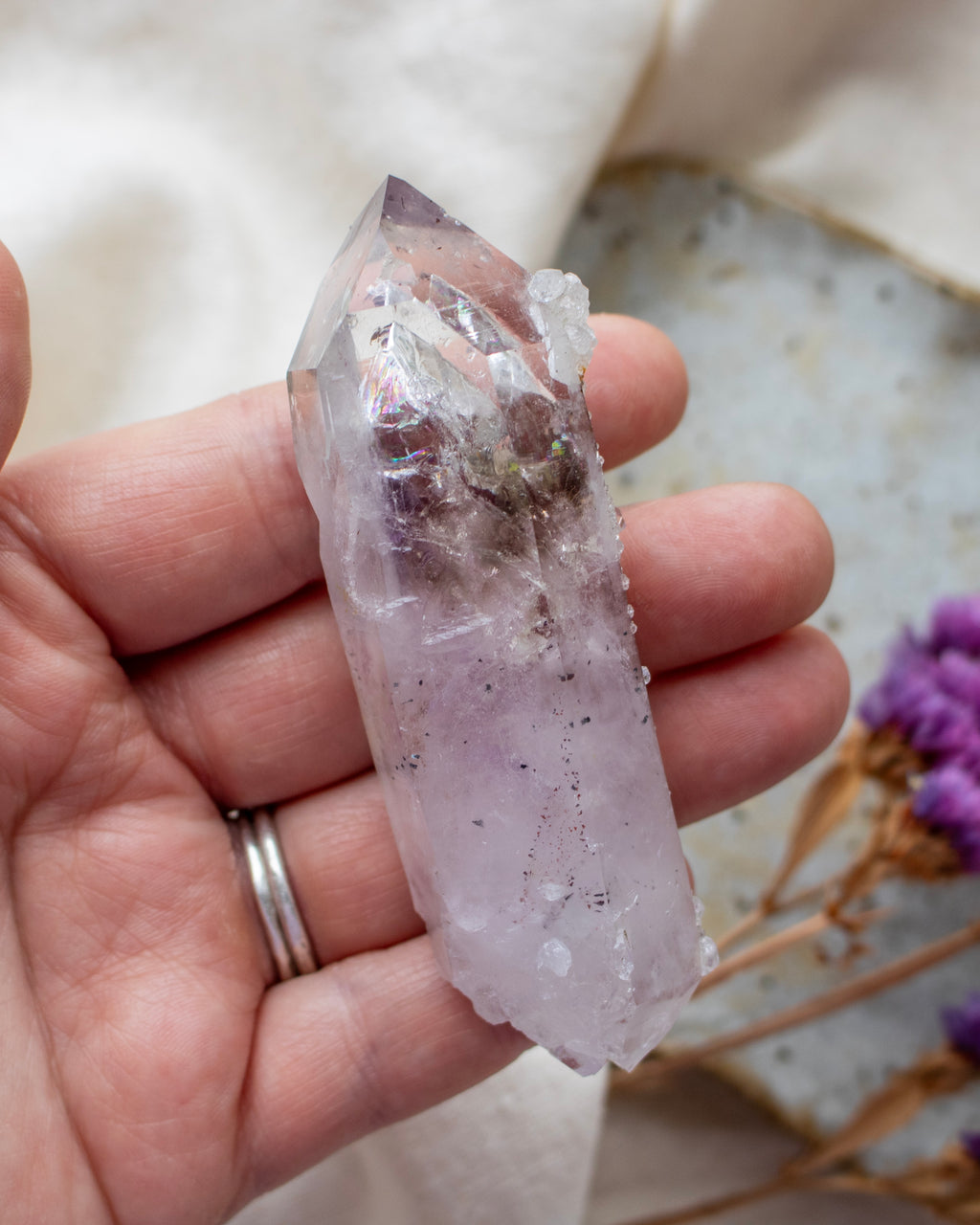 Hand holding a clear crystal with purple undertones against a blurred natural background