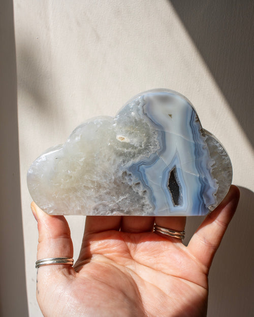 Cloud-shaped agate stone held in a hand against a neutral background
