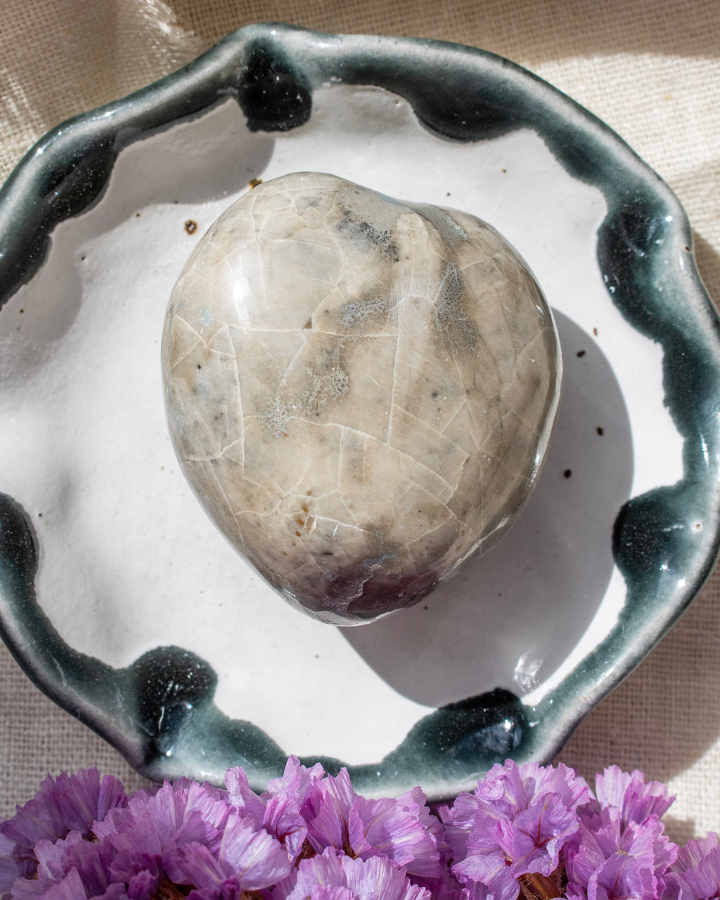 Heart-shaped stone on a ceramic dish with purple flowers in the foreground
