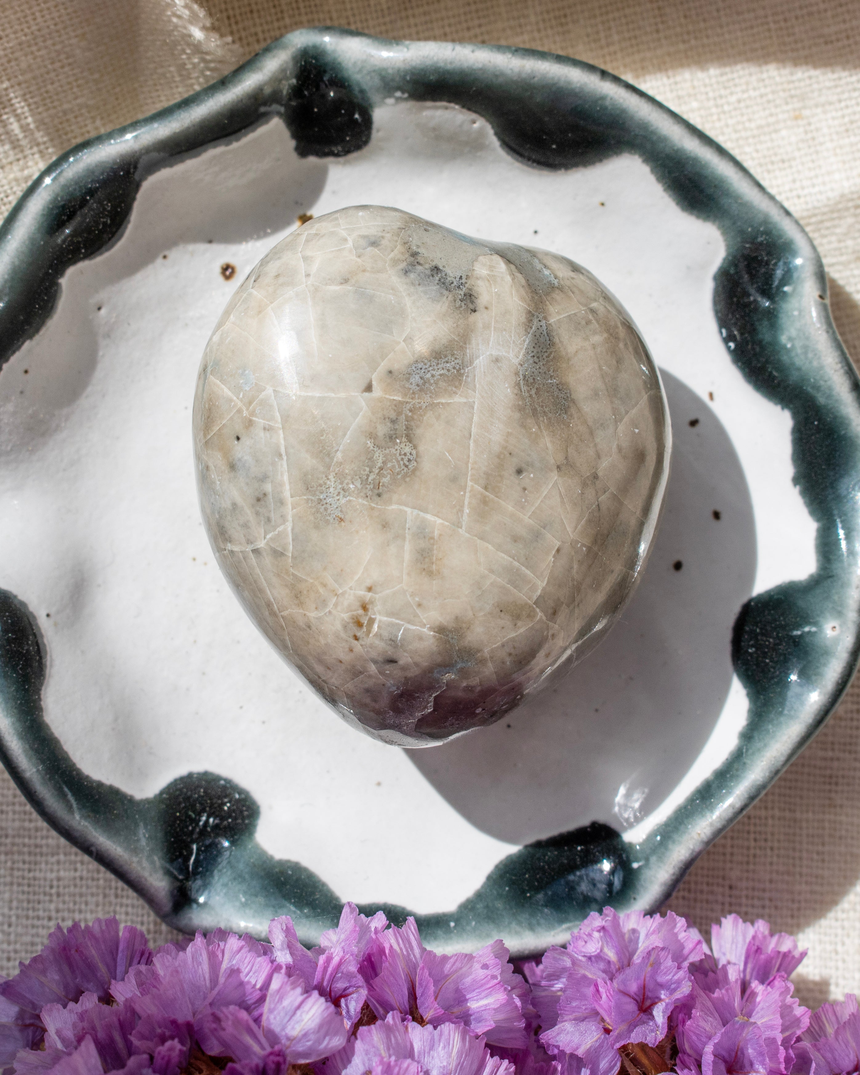 Heart-shaped stone on a ceramic dish with purple flowers in the foreground