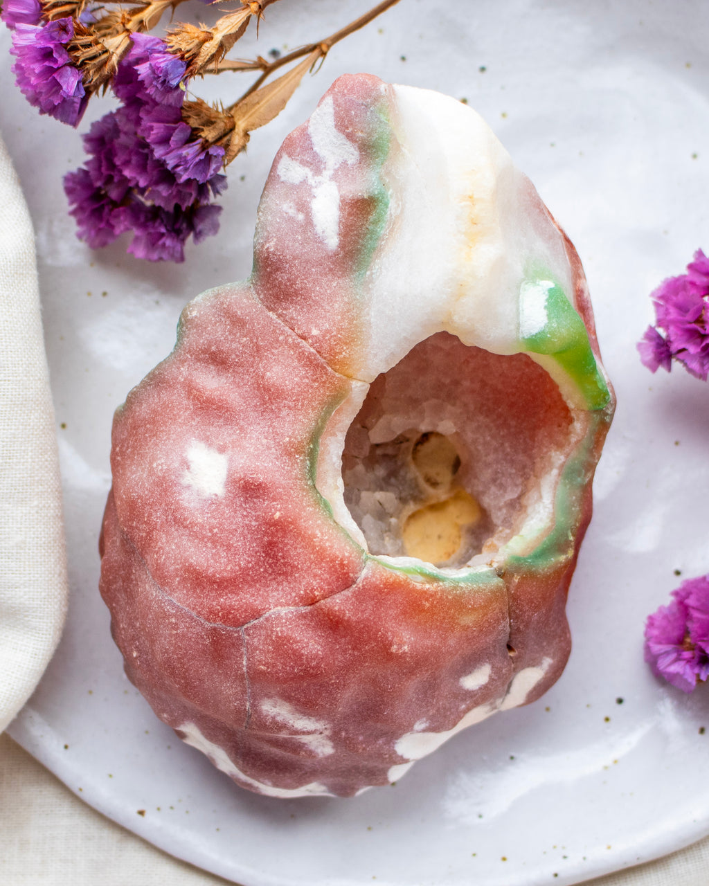 Decorative stone with a central cavity on a white plate with purple flowers.