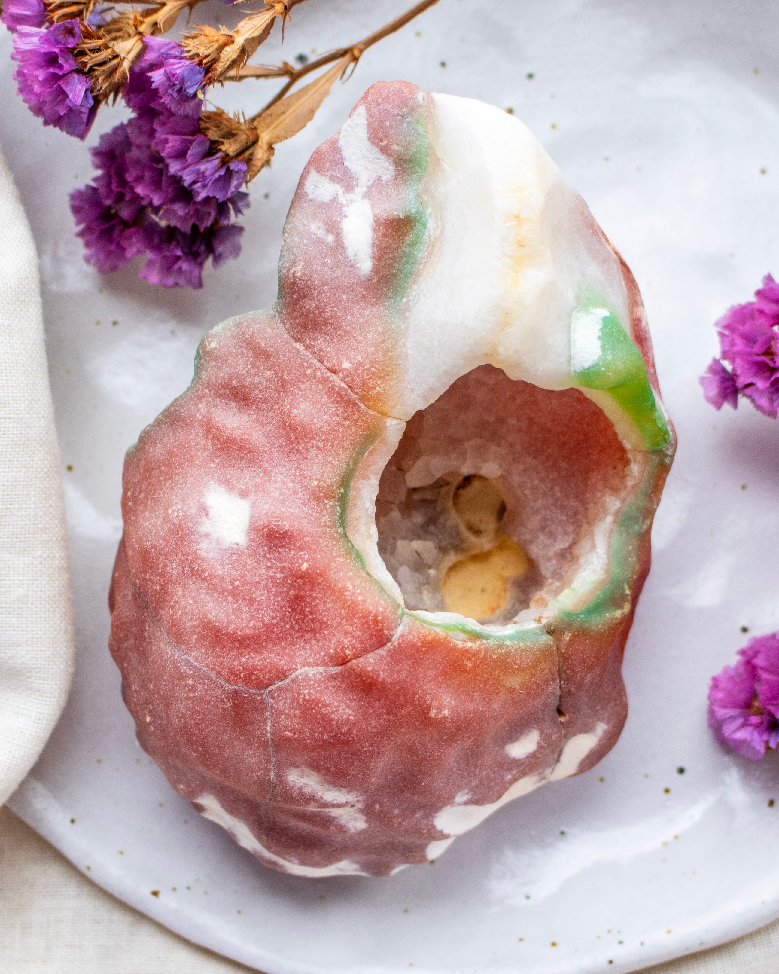 Decorative stone with a central cavity on a white plate with purple flowers.