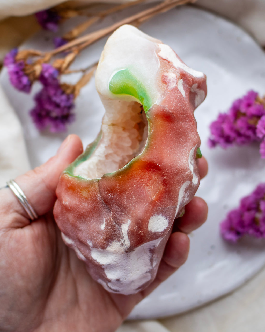 Hand holding a colorful agate stone with a floral background