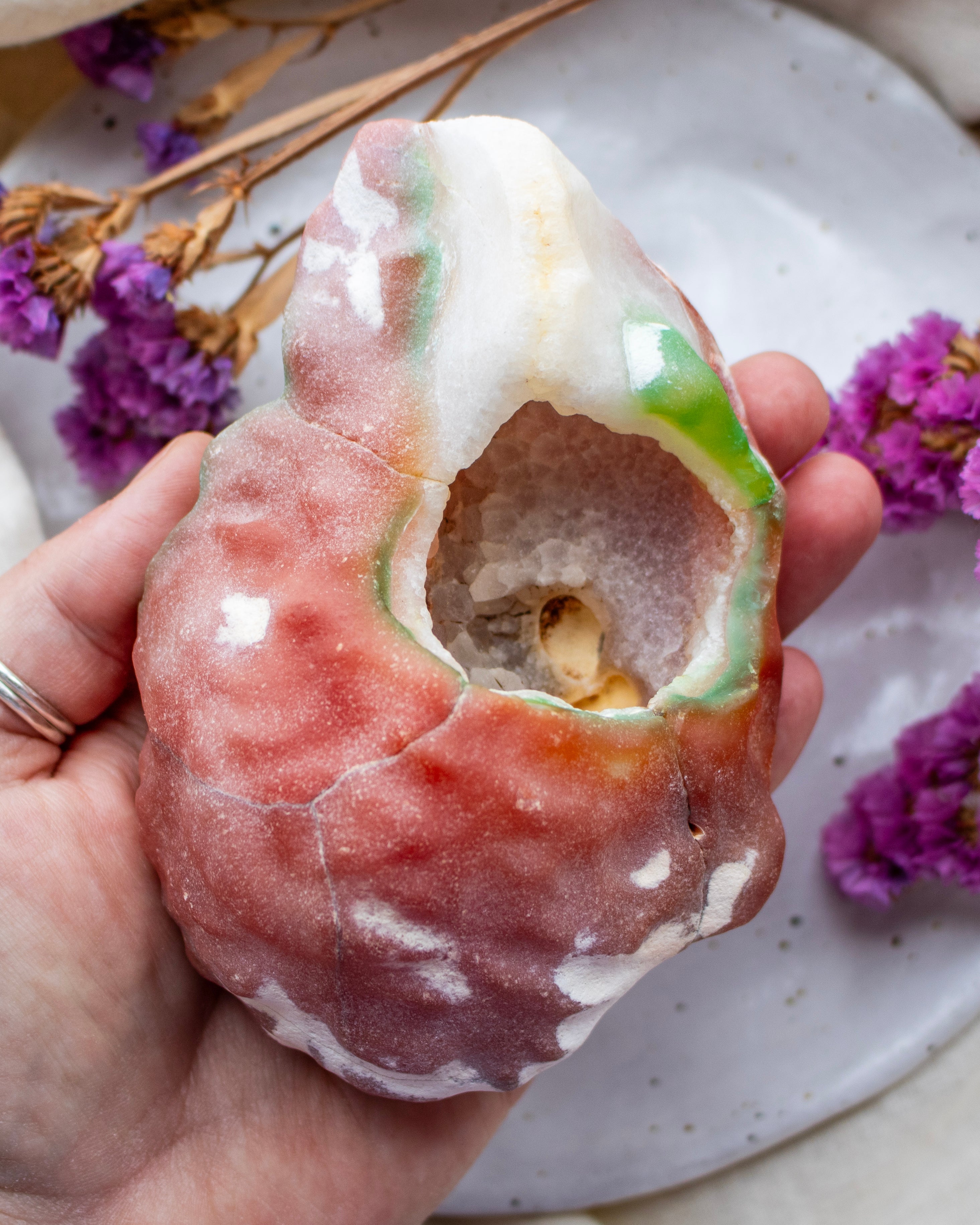 Hand holding a unique agate with a textured surface, surrounded by purple flowers on a speckled plate.