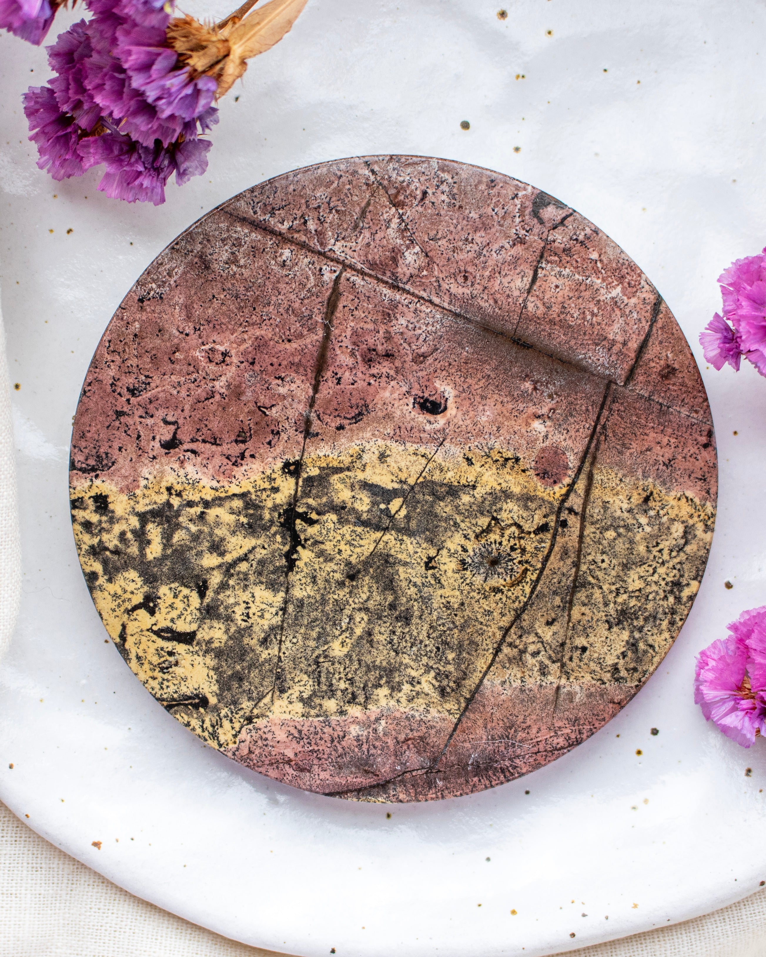 Round stone coaster with a gradient design on a white surface with purple flowers.