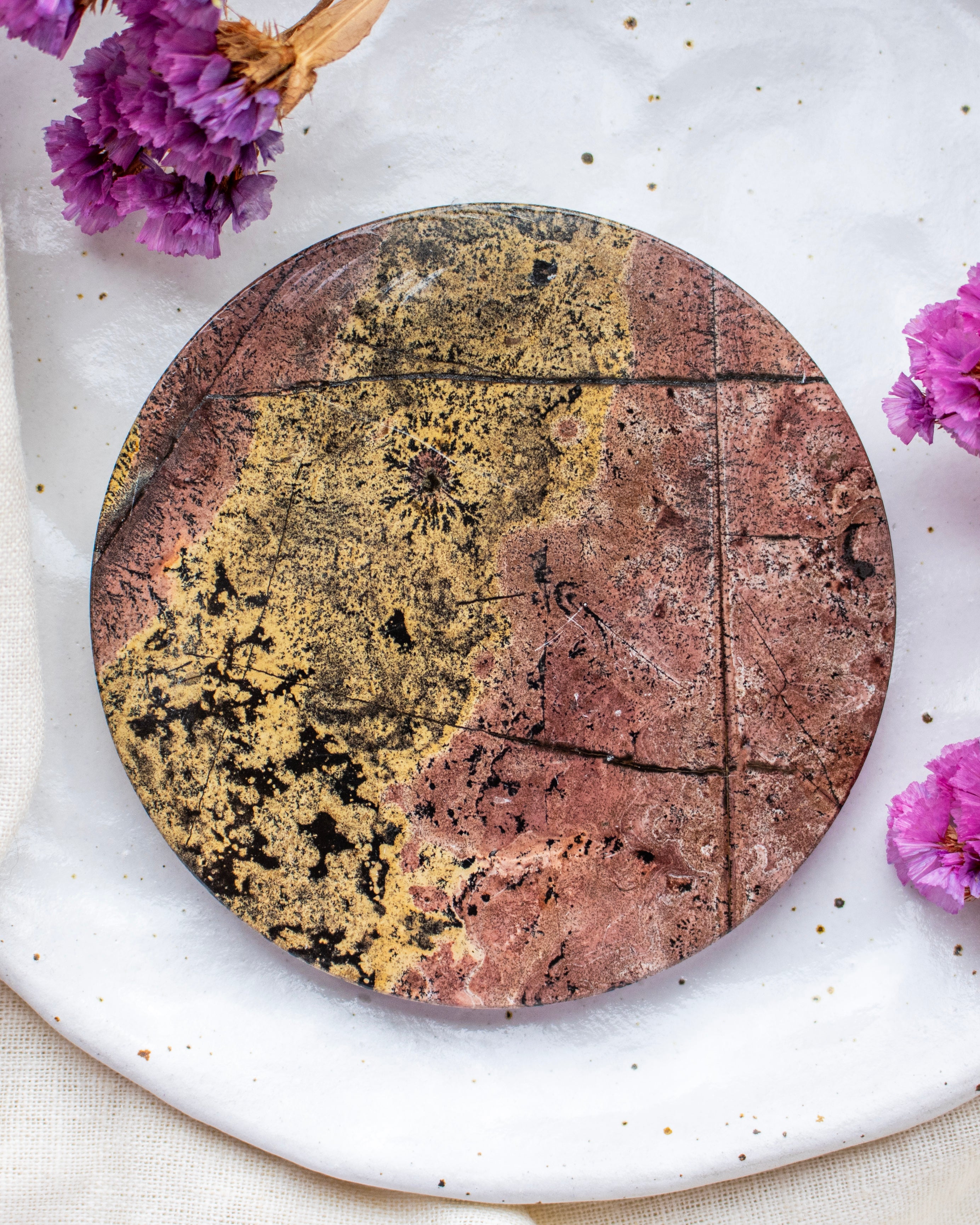 Round stone coaster with a marbled design on a white surface with purple flowers.