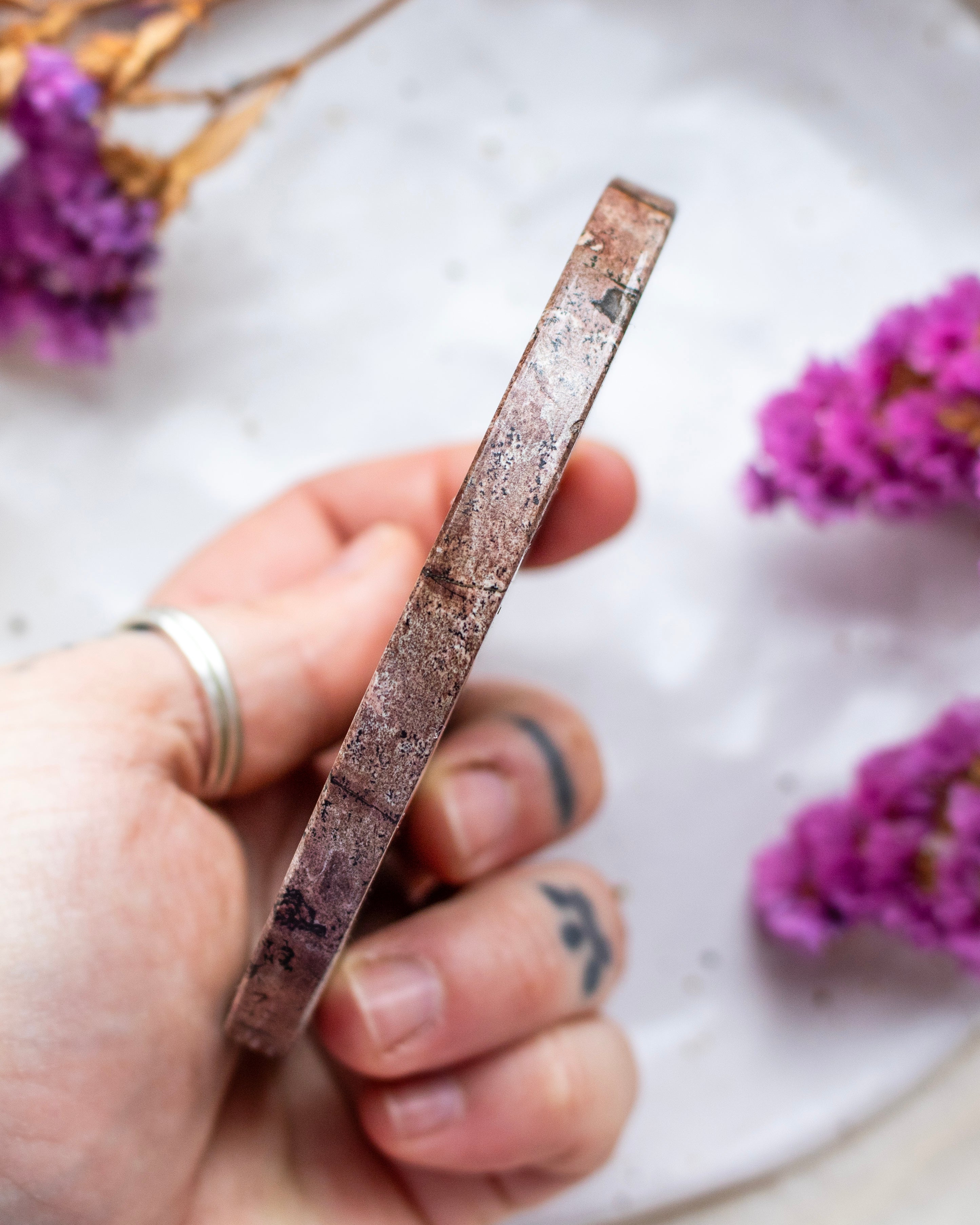 Hand holding a flat disc with purple flowers in the background