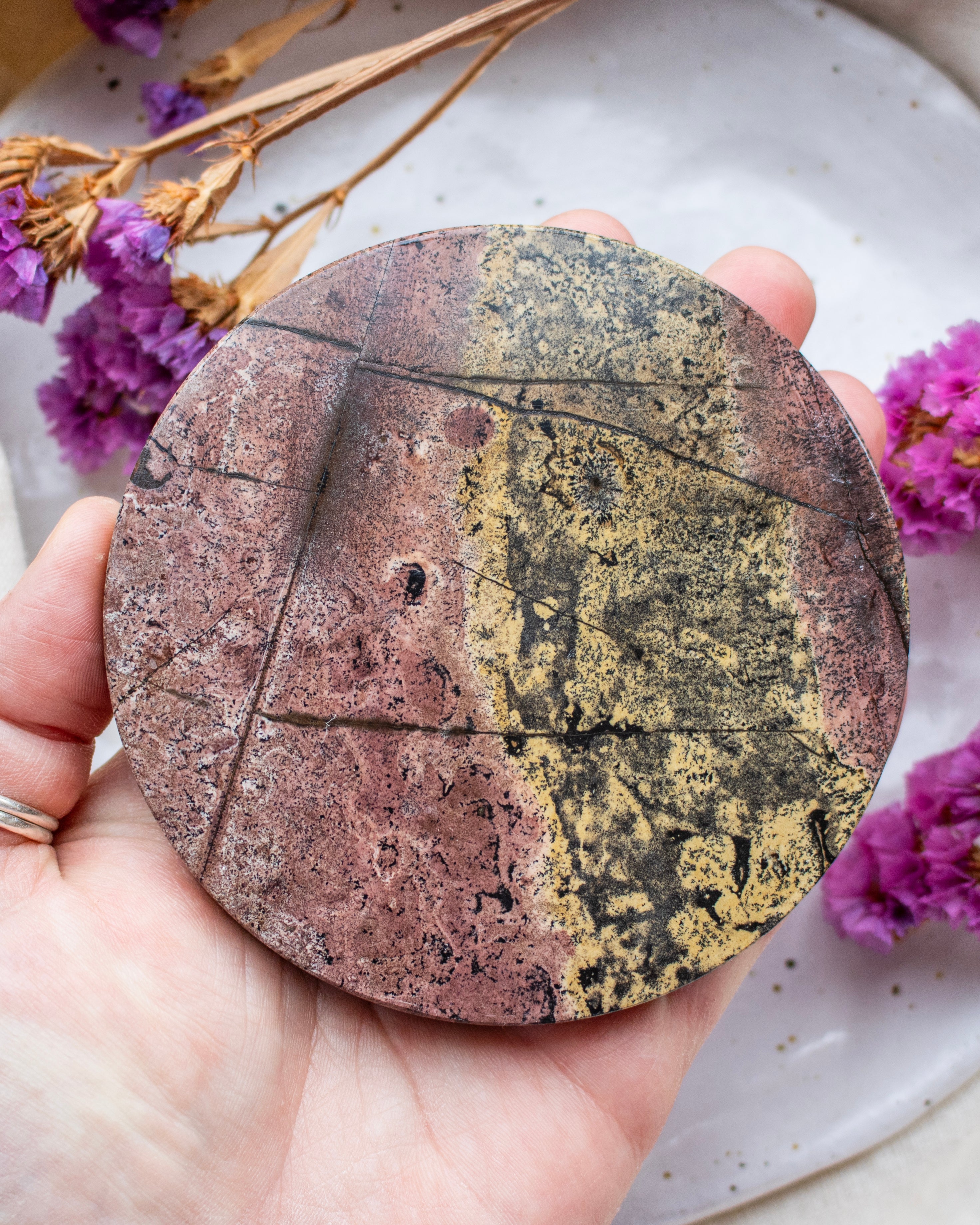 Round, multicolored stone held in a hand with purple flowers in the background