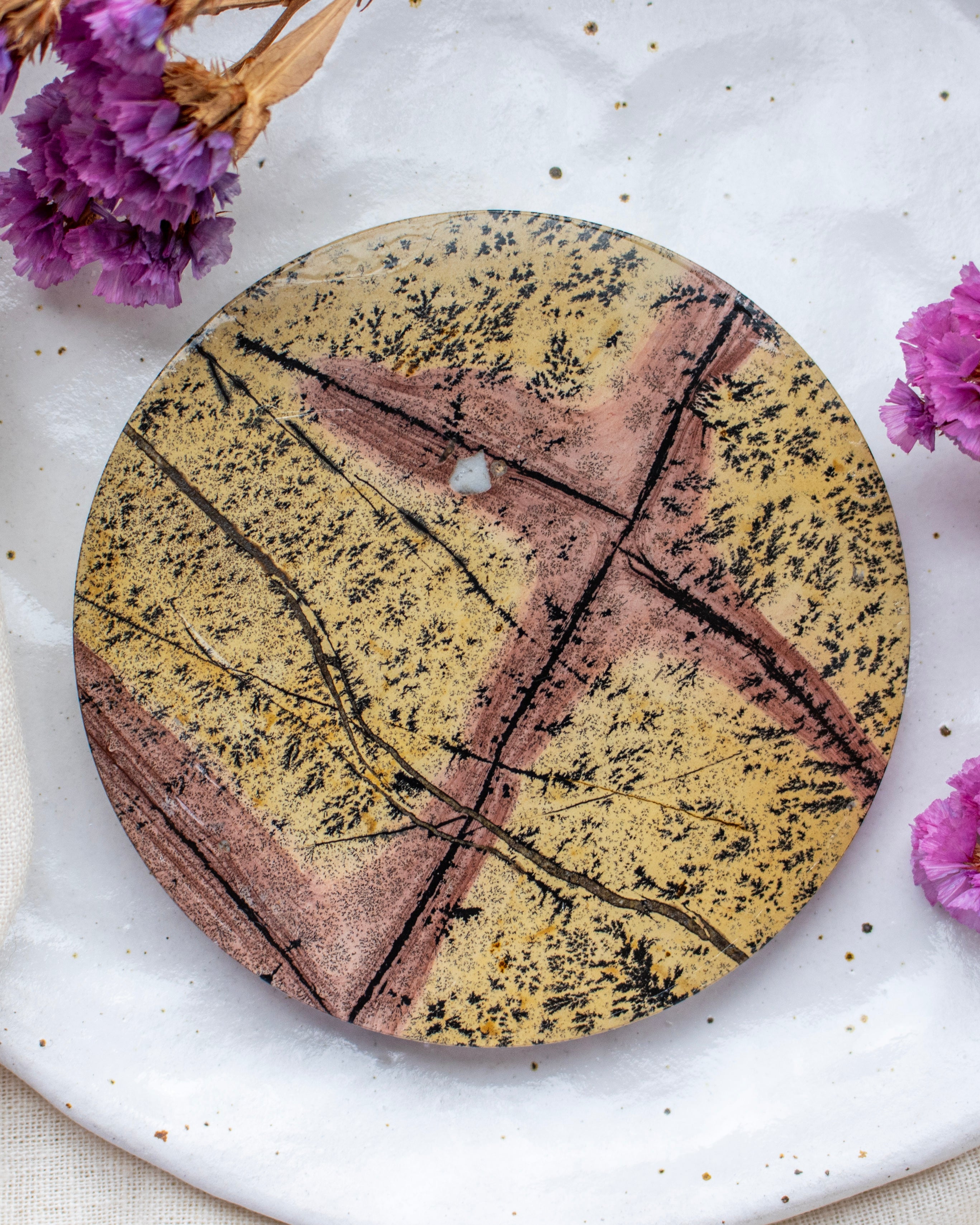 Round decorative plate with a geometric pattern on a white surface with purple flowers.