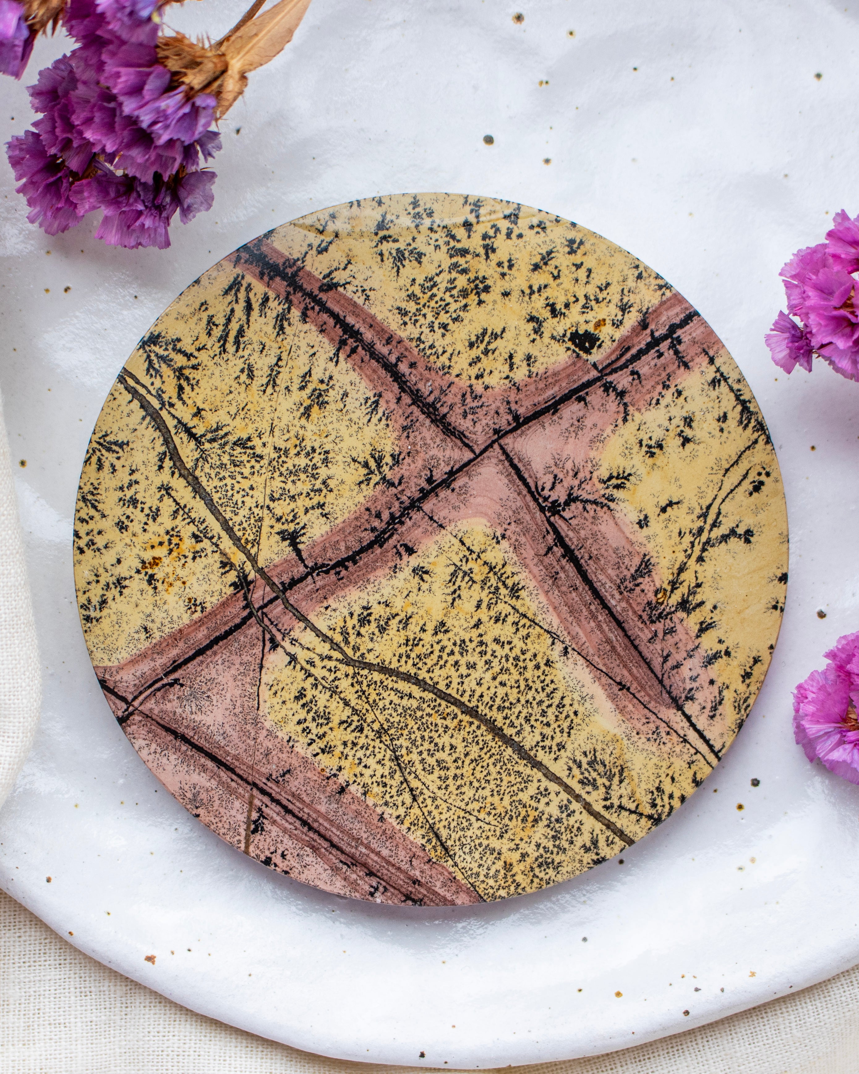 Round stone coaster with artistic design on a white surface with purple flowers