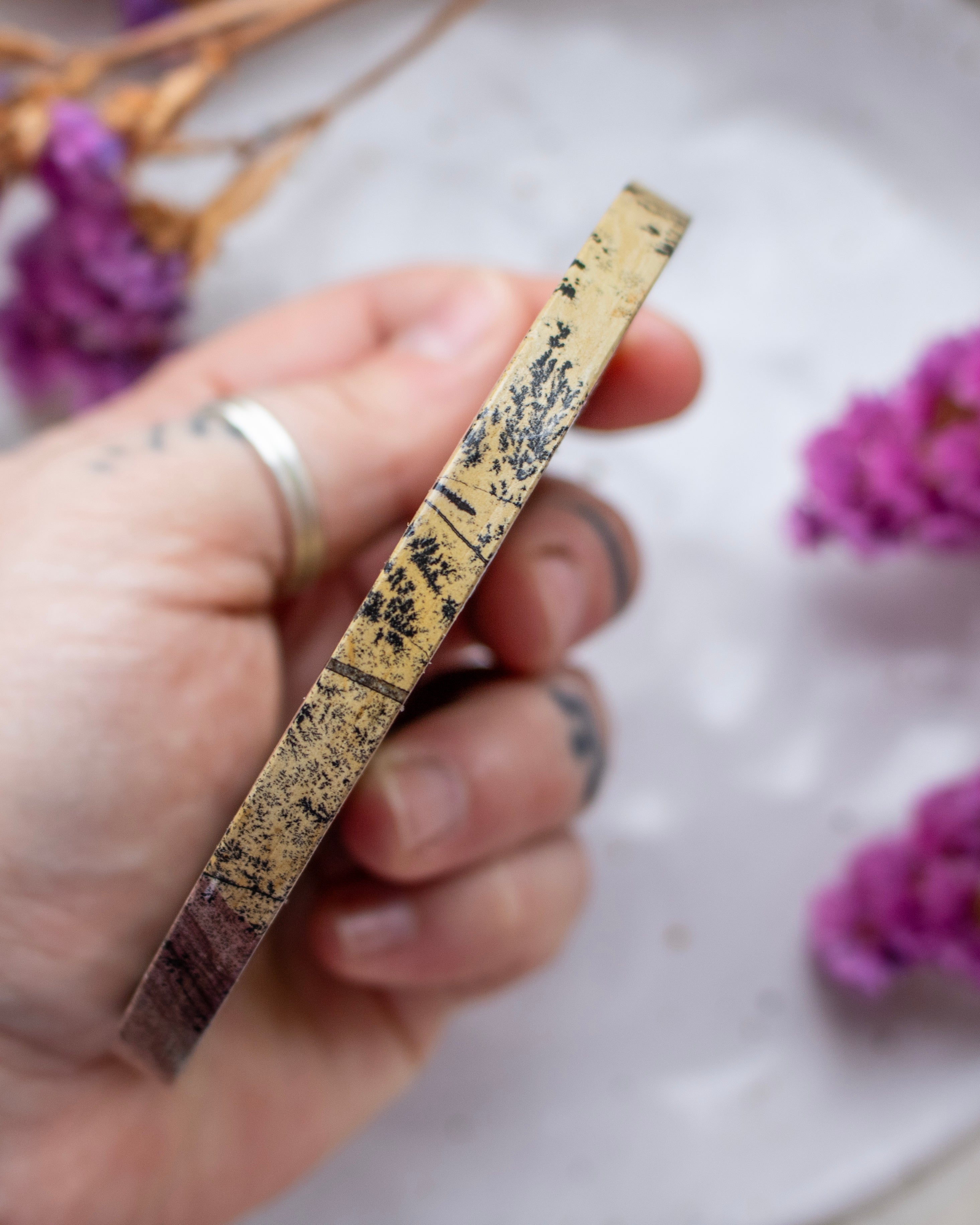 Hand holding a flat disc with floral decorations against a blurred background of purple flowers.