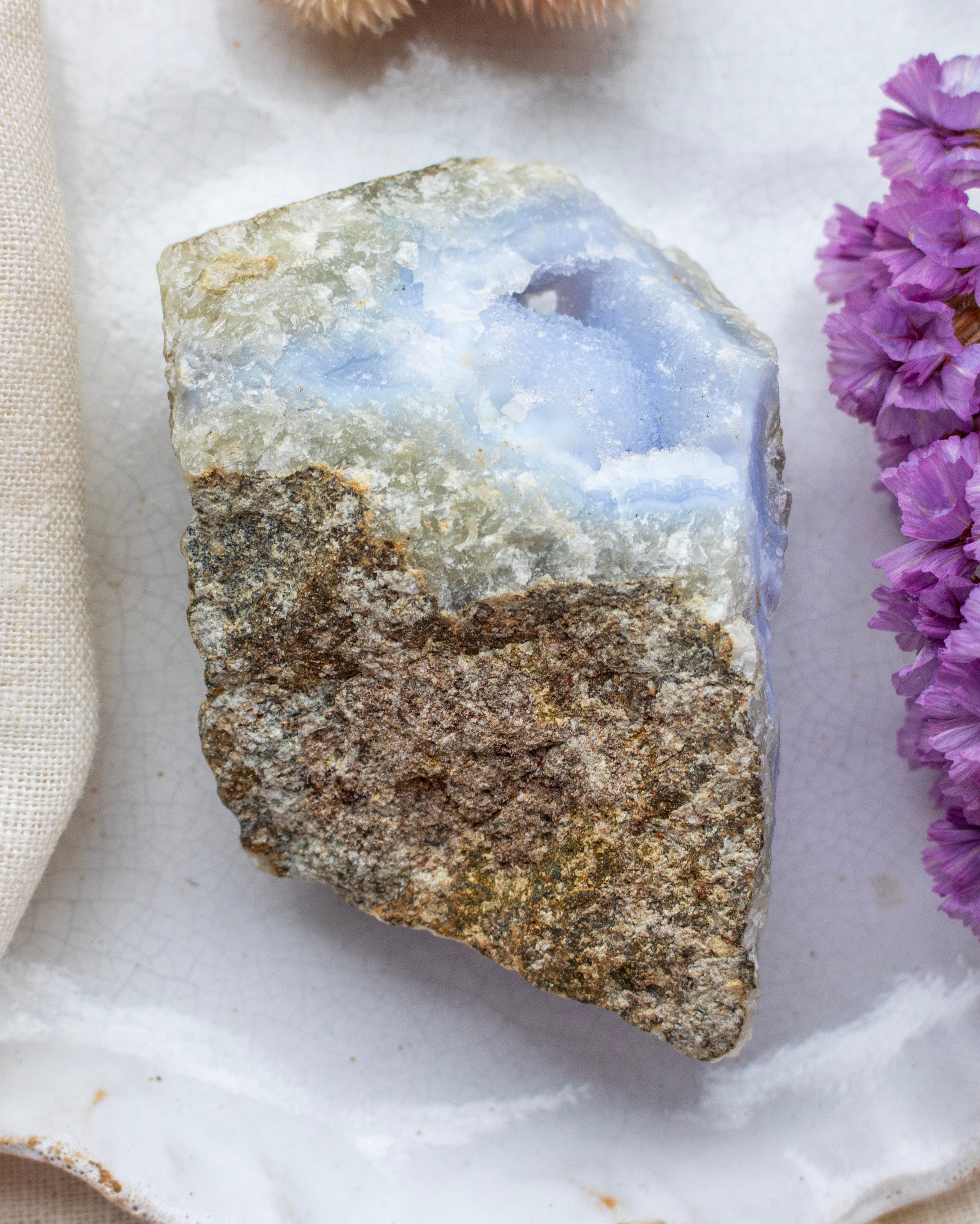 Raw crystal stone on a marble surface with purple flowers