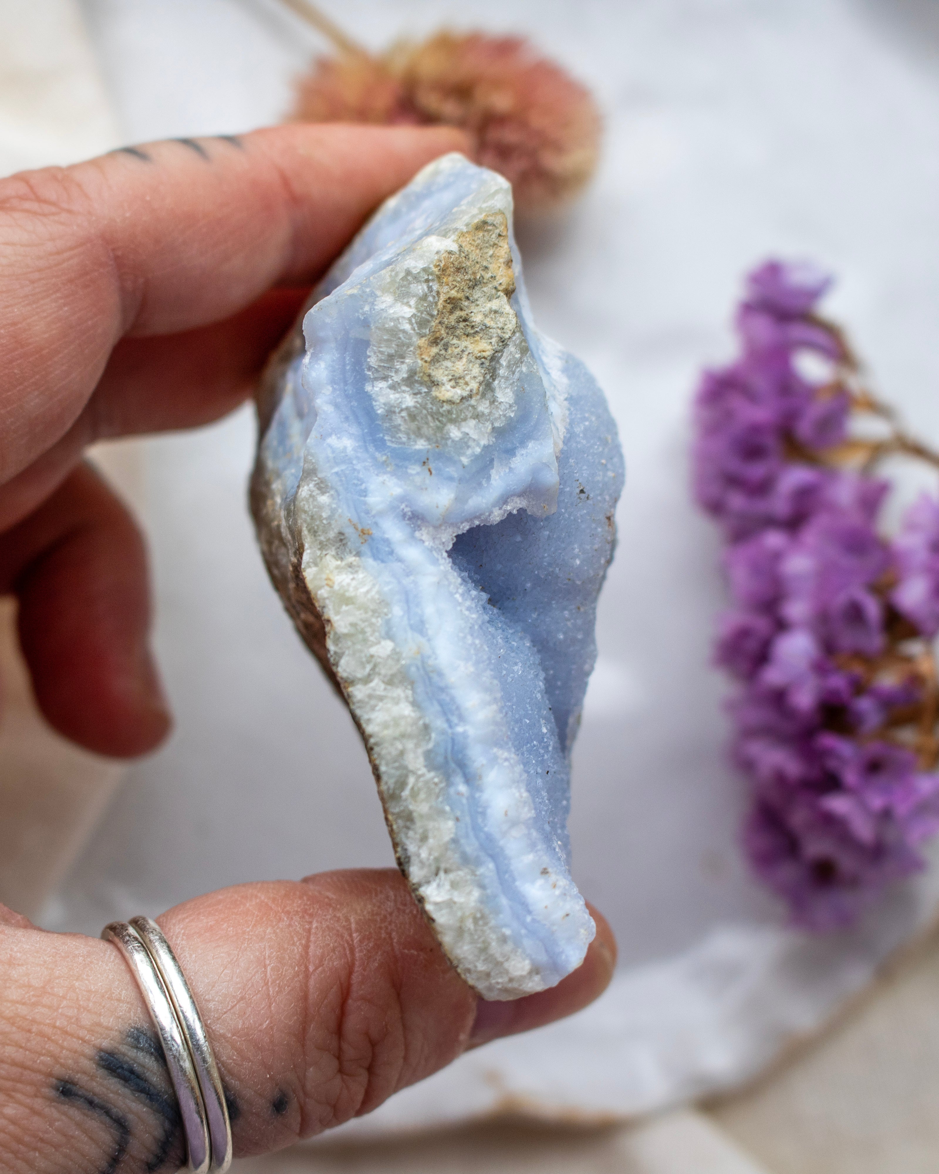 Hand holding a blue and white geode crystal with purple flowers in the background