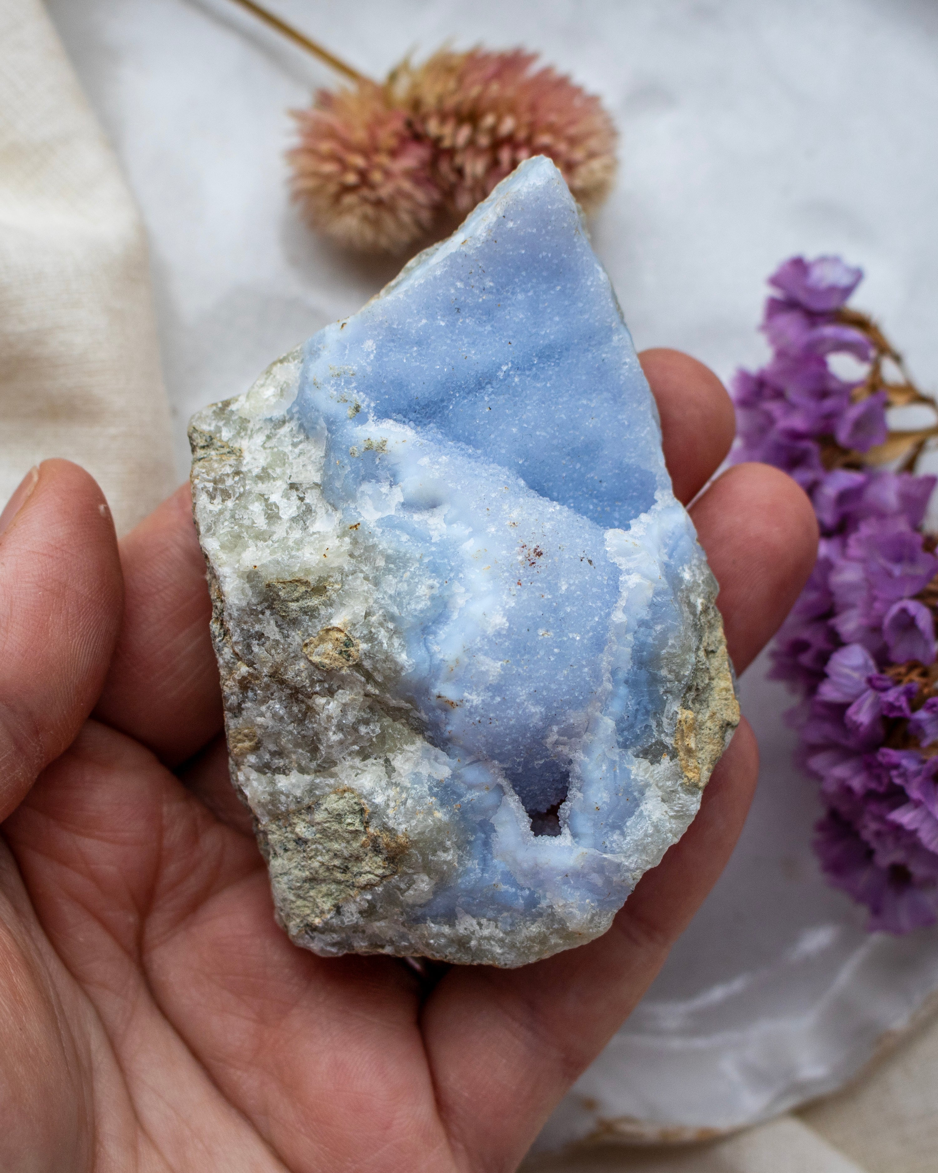Hand holding a blue crystal with purple flowers in the background