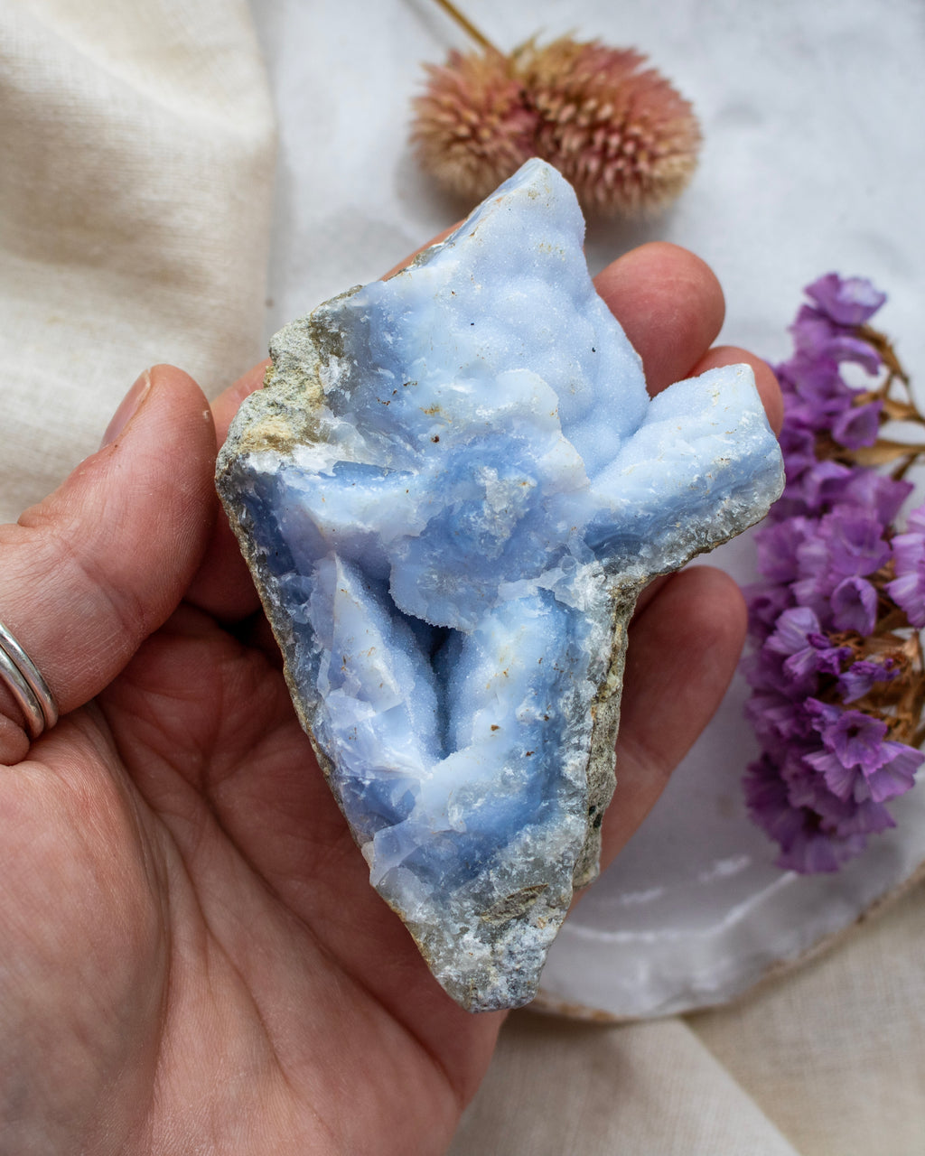 Hand holding a blue geode crystal with flowers in the background