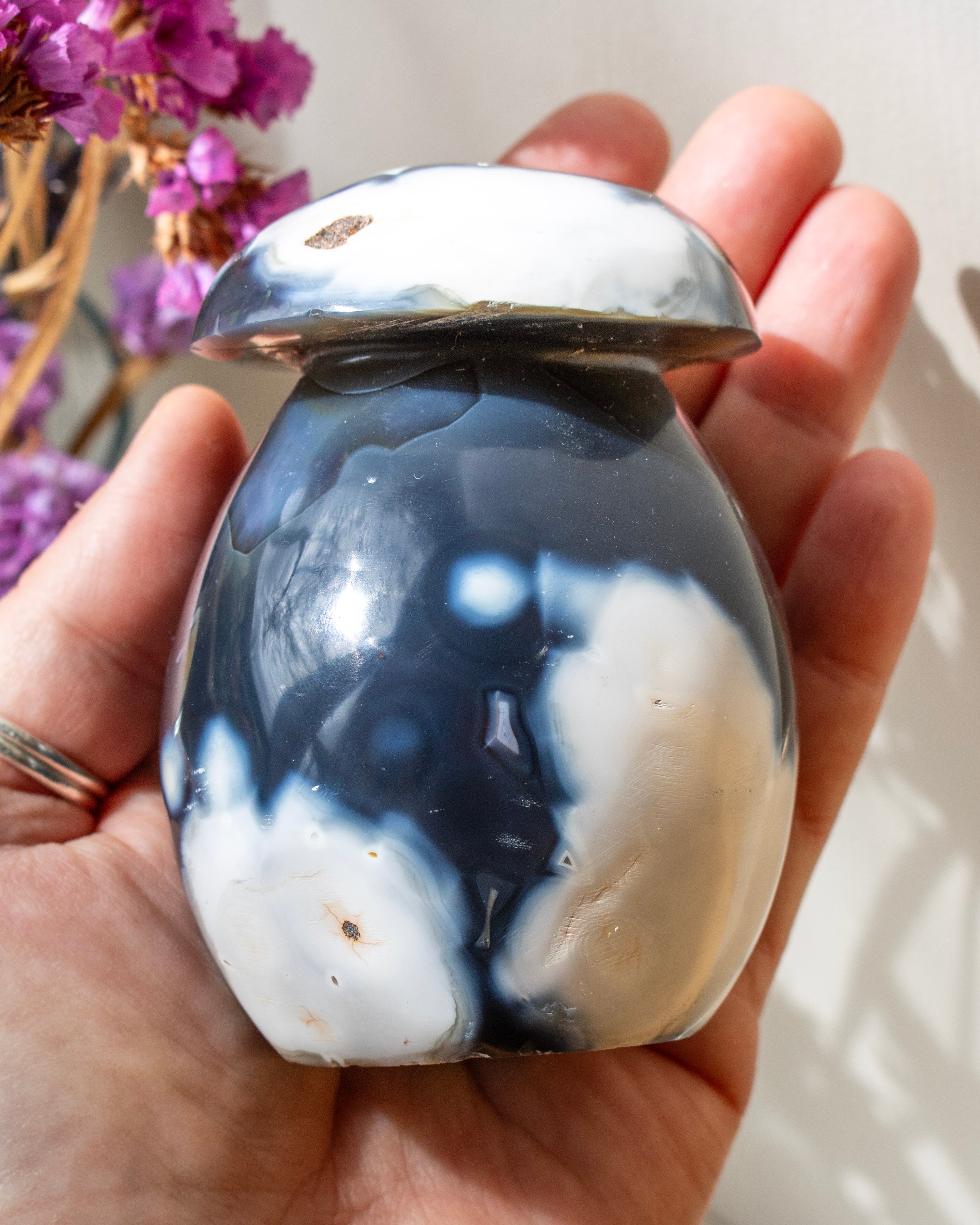 Marbled agate held in a hand, with blurred purple flowers in the background.