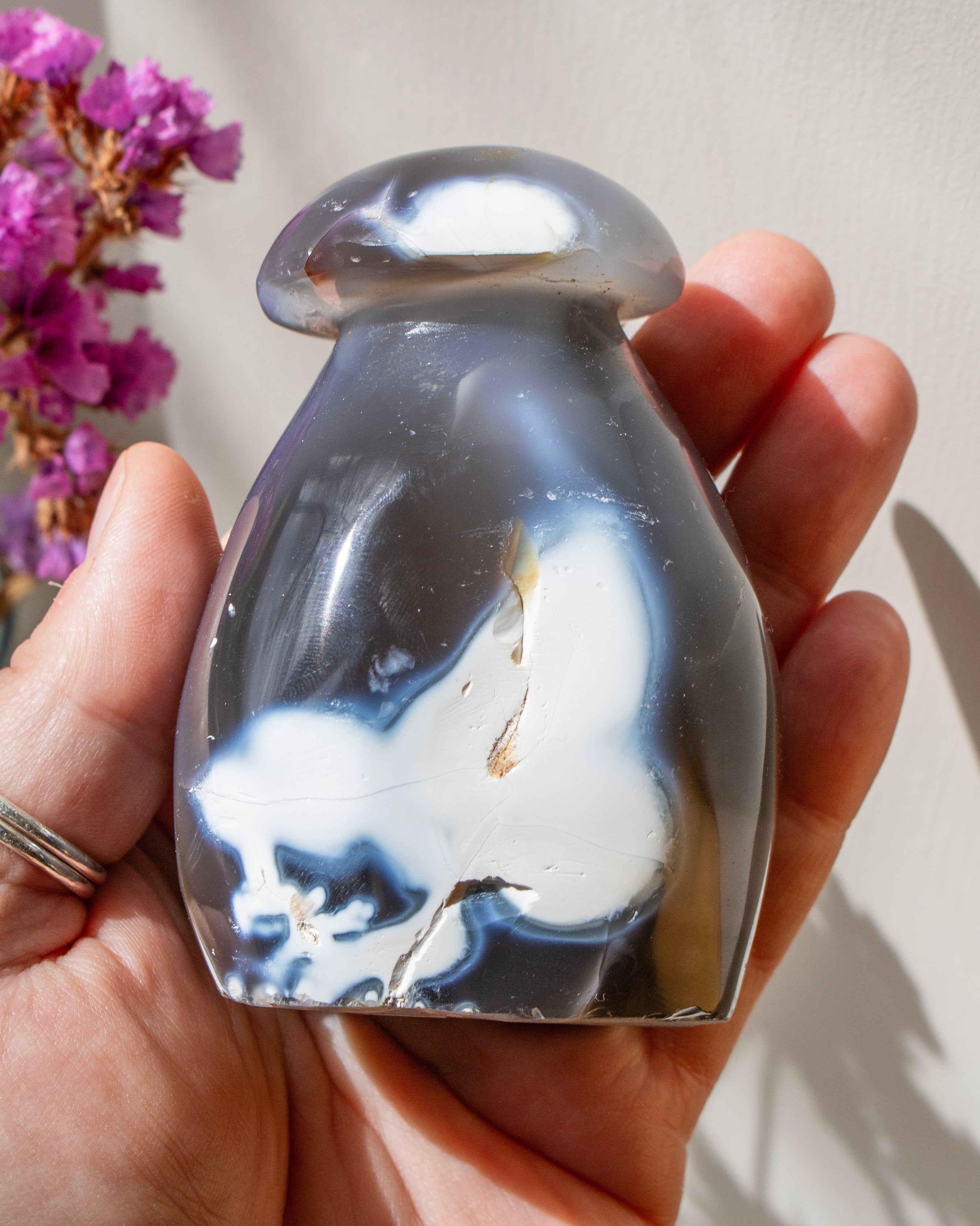 Hand holding a marbled stone with a blurred purple flower in the background