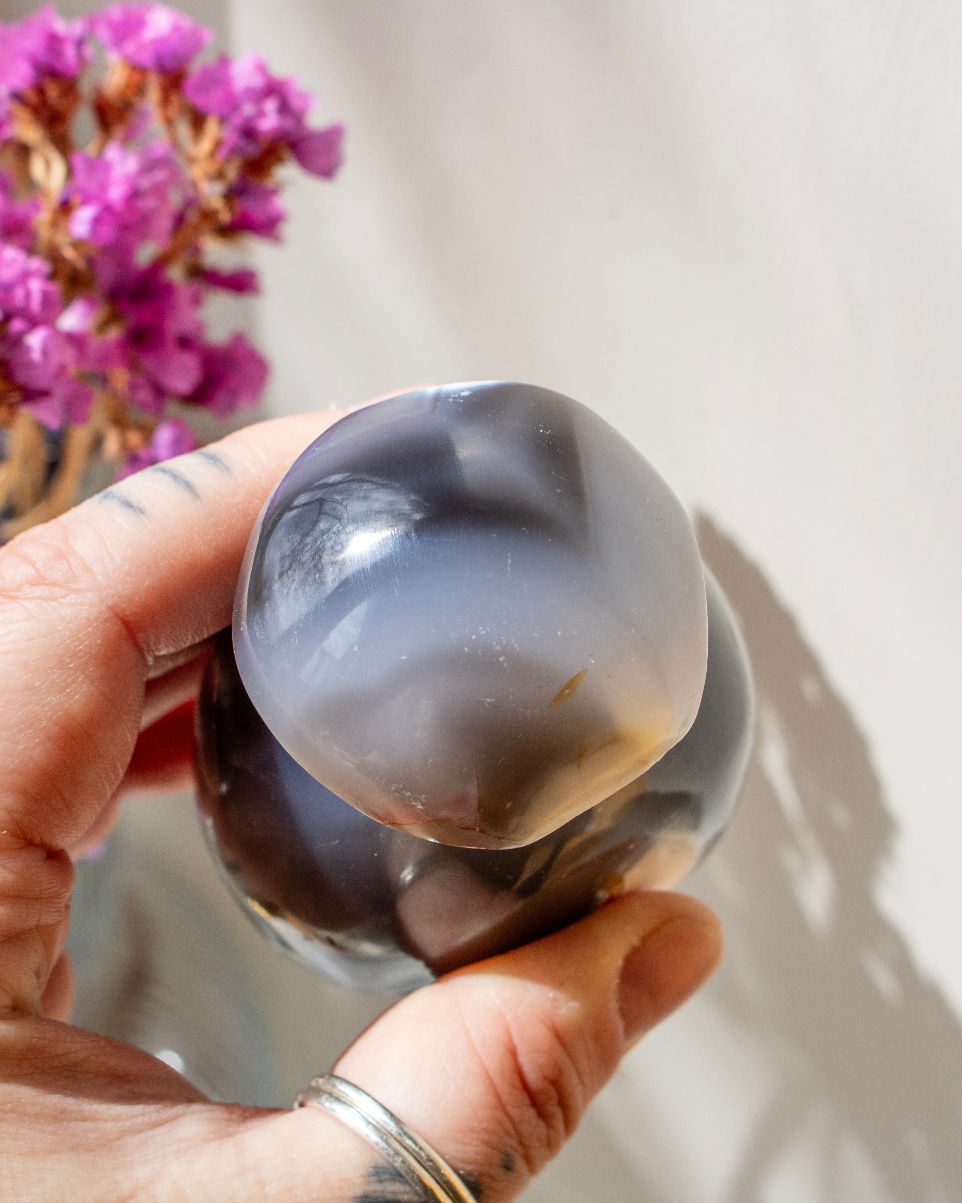 Hand holding a polished agate stone with a blurred background of pink flowers